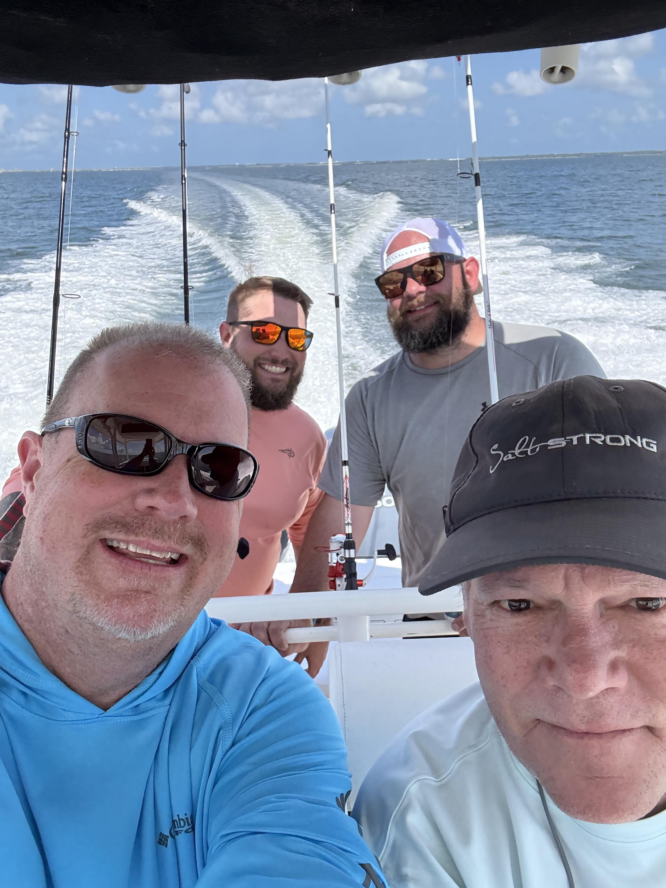 Four men smile and pose for a selfie while fishing on a boat in the ocean.