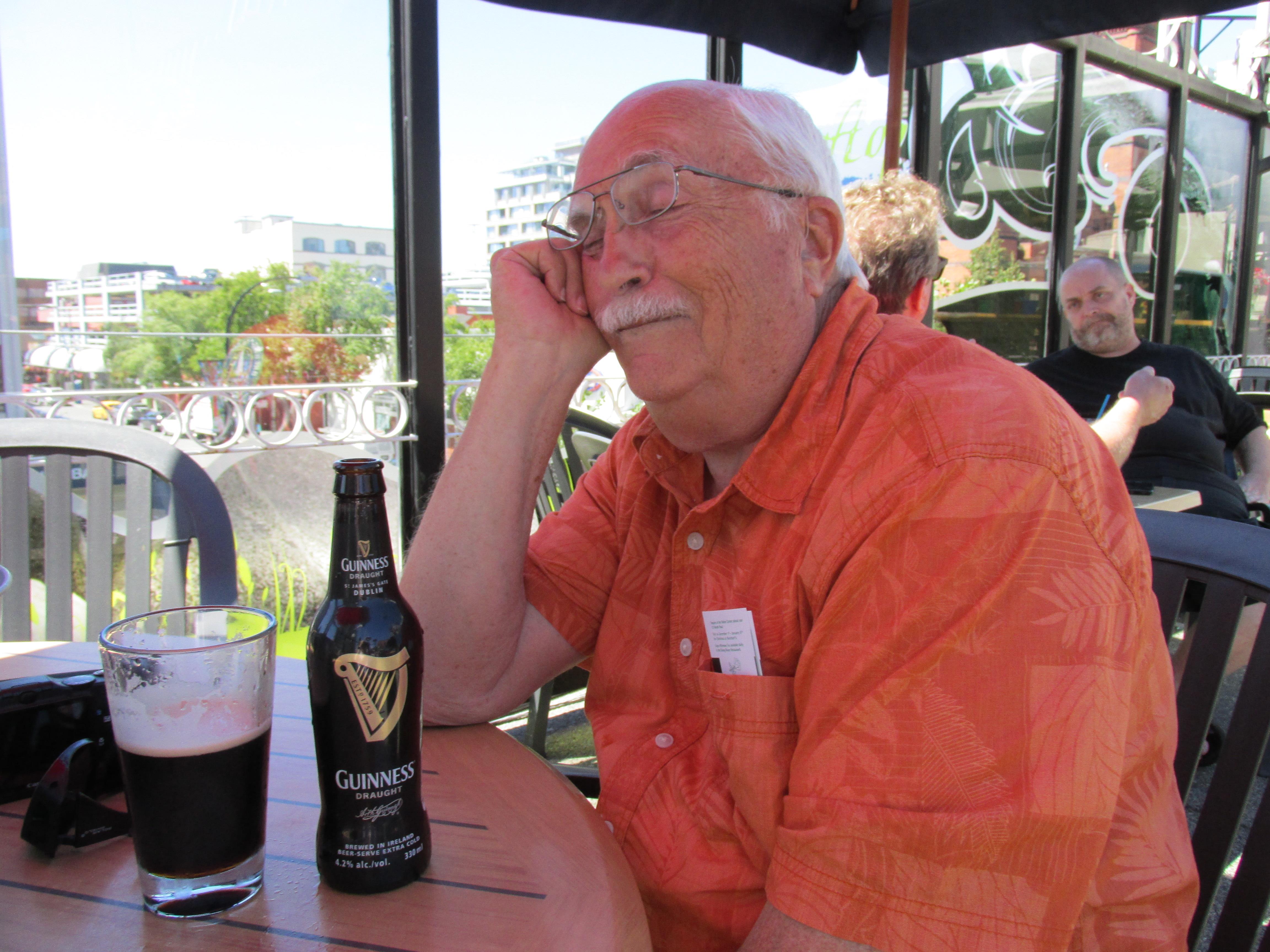 A man sitting at a table with a beer and a glass