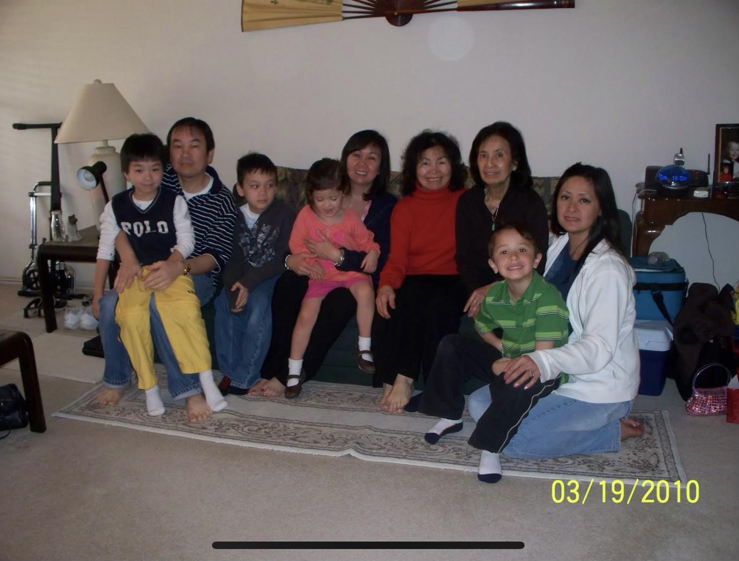 Group of children and adults sit together on a rug in a living room.