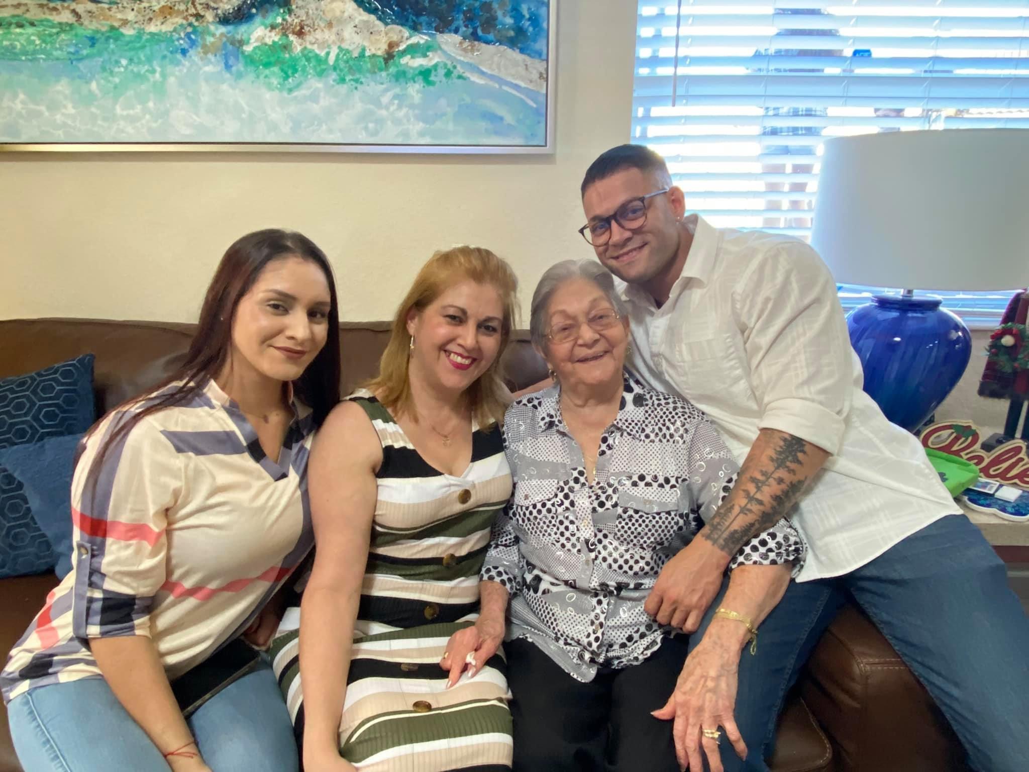 Four family members sit on a couch smiling and enjoying their time together at home.