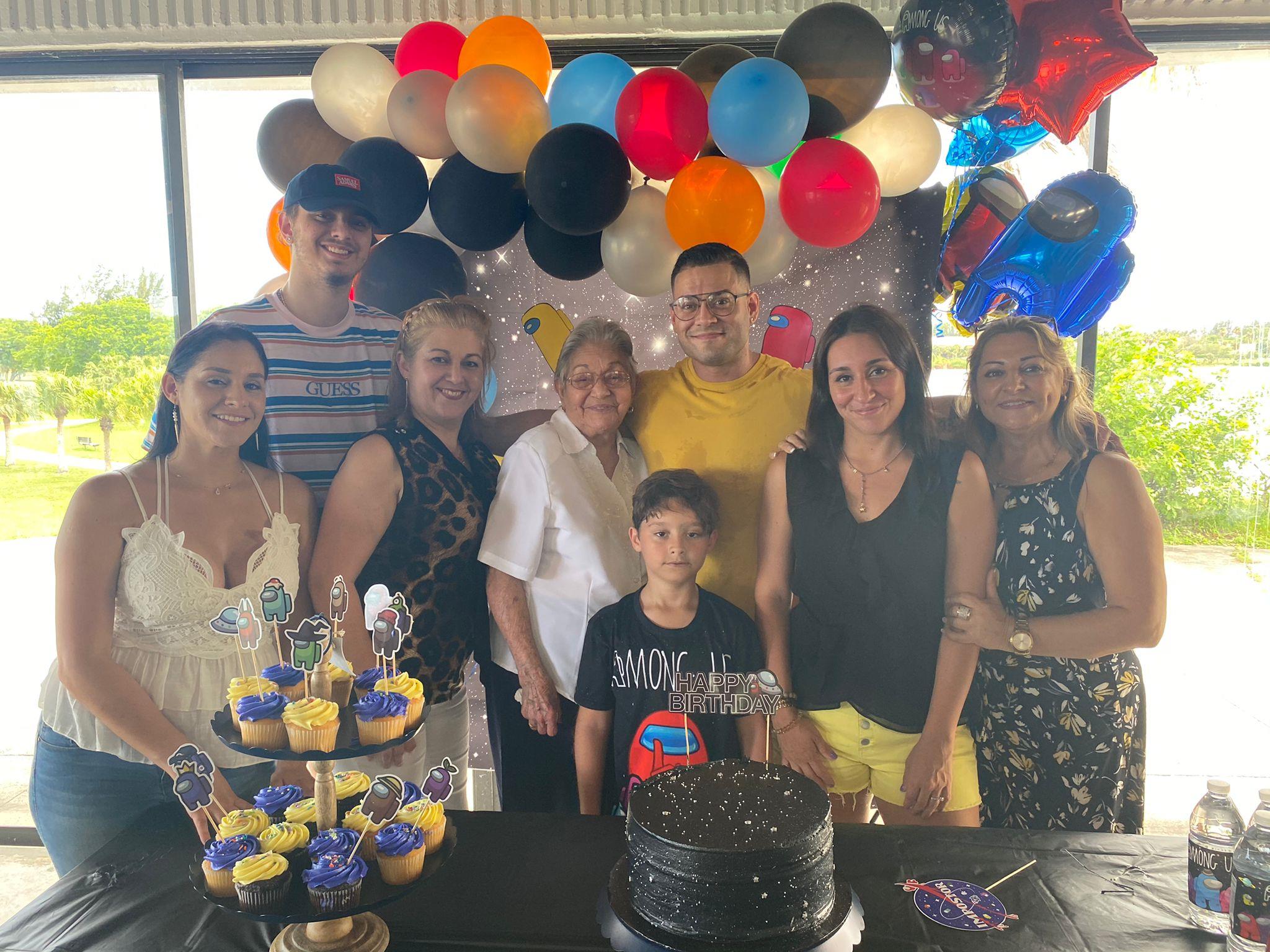 People gather at a location for a birthday party with a cake and colorful decorations.