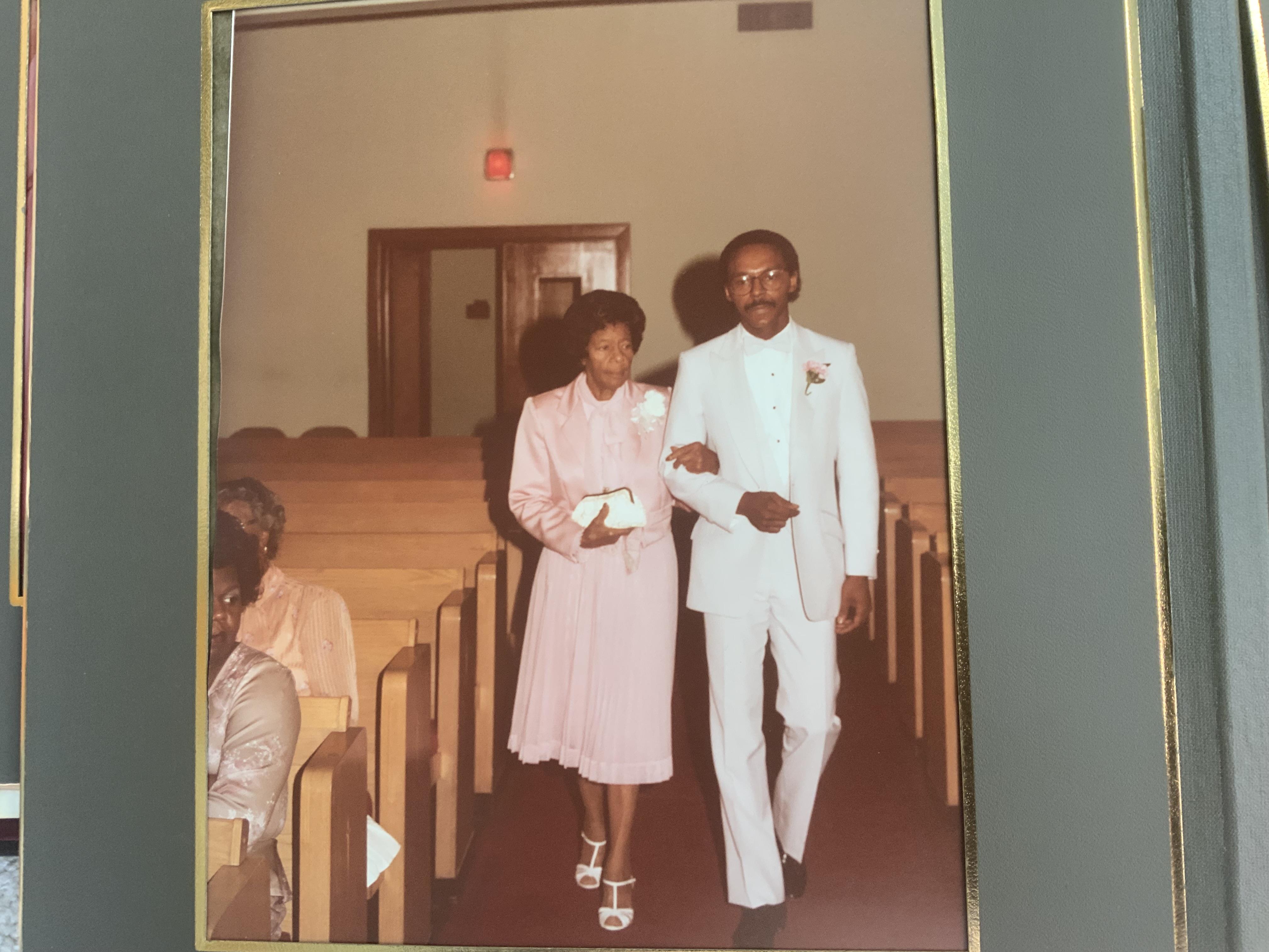 A man and a woman walk together down the aisle of a church during a formal event.