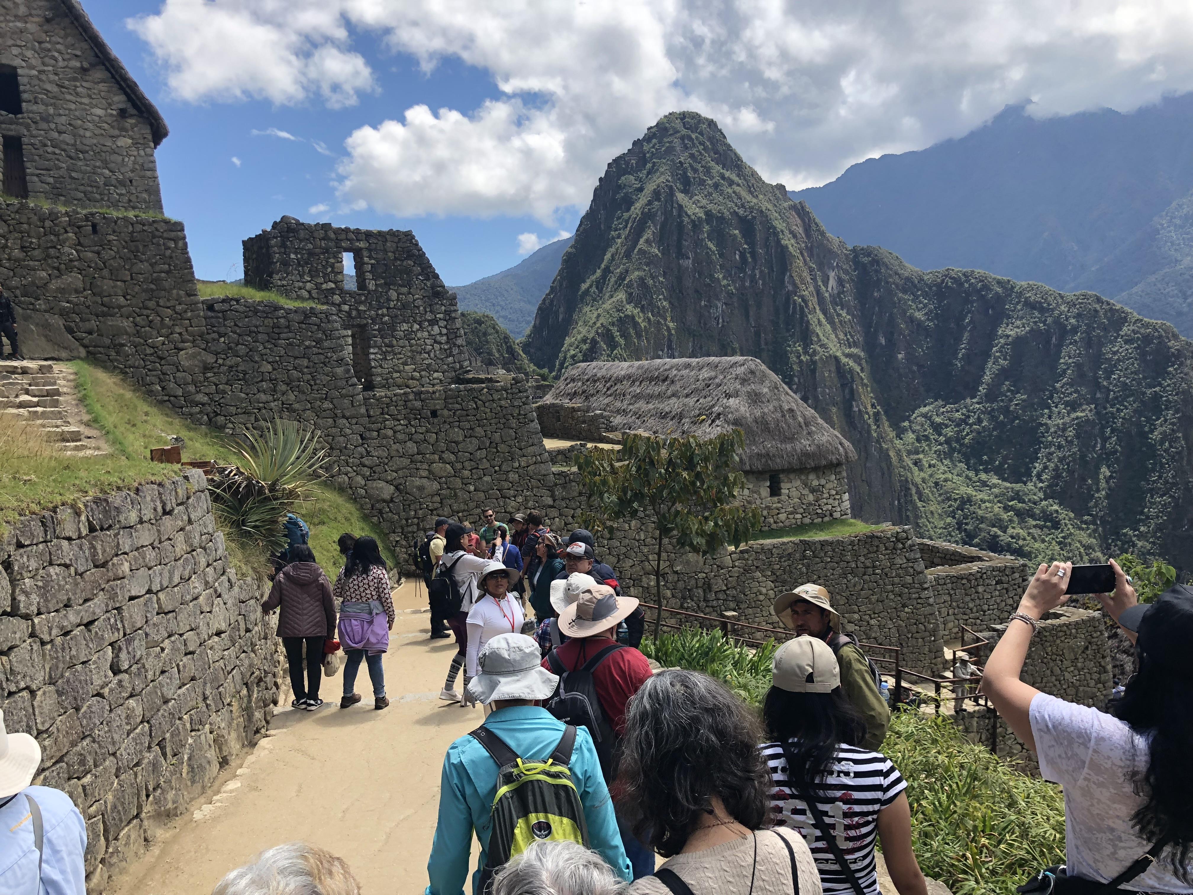 A group of people walking on a path with stone buildings and mountains