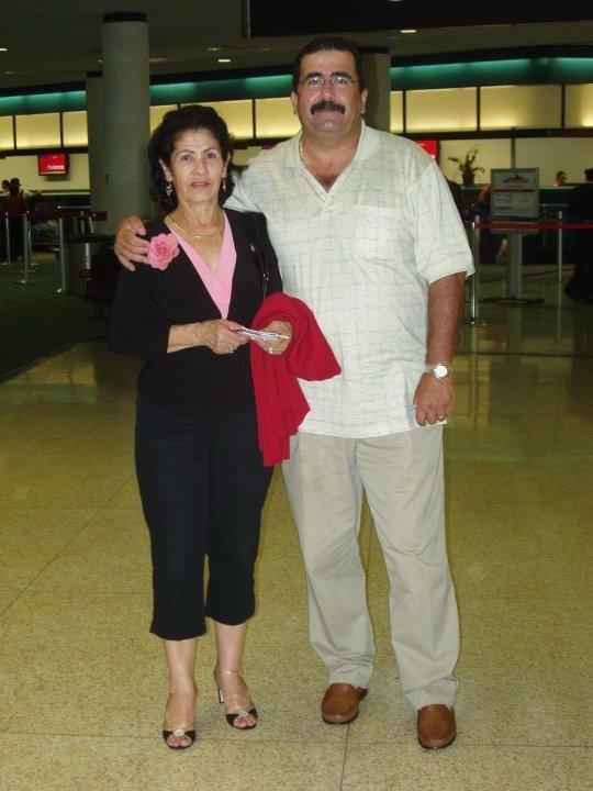 Two people pose for a picture inside an airport while holding travel documents.