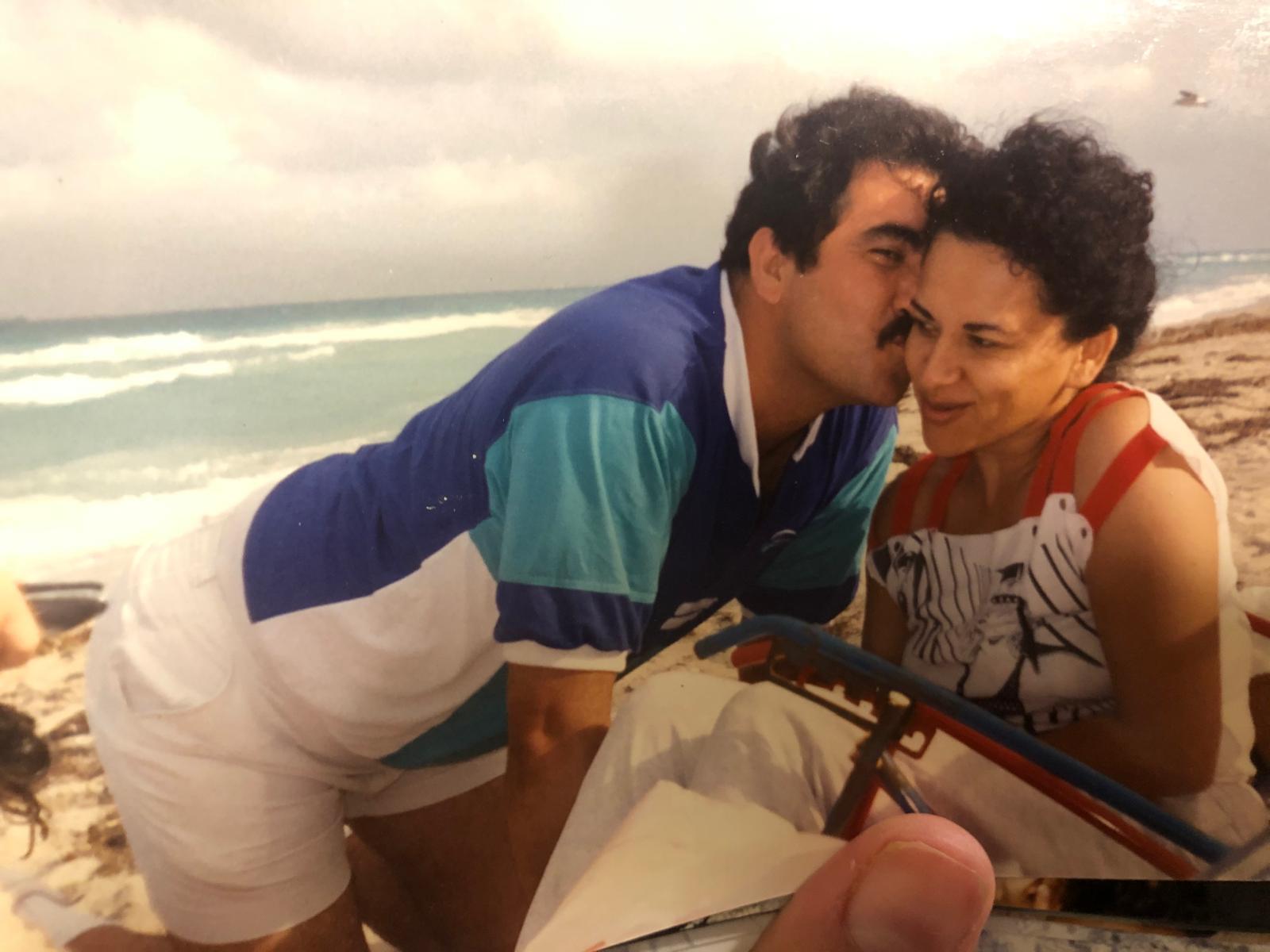 A couple smiles and shares a close moment at the beach on a cloudy day by the sea.