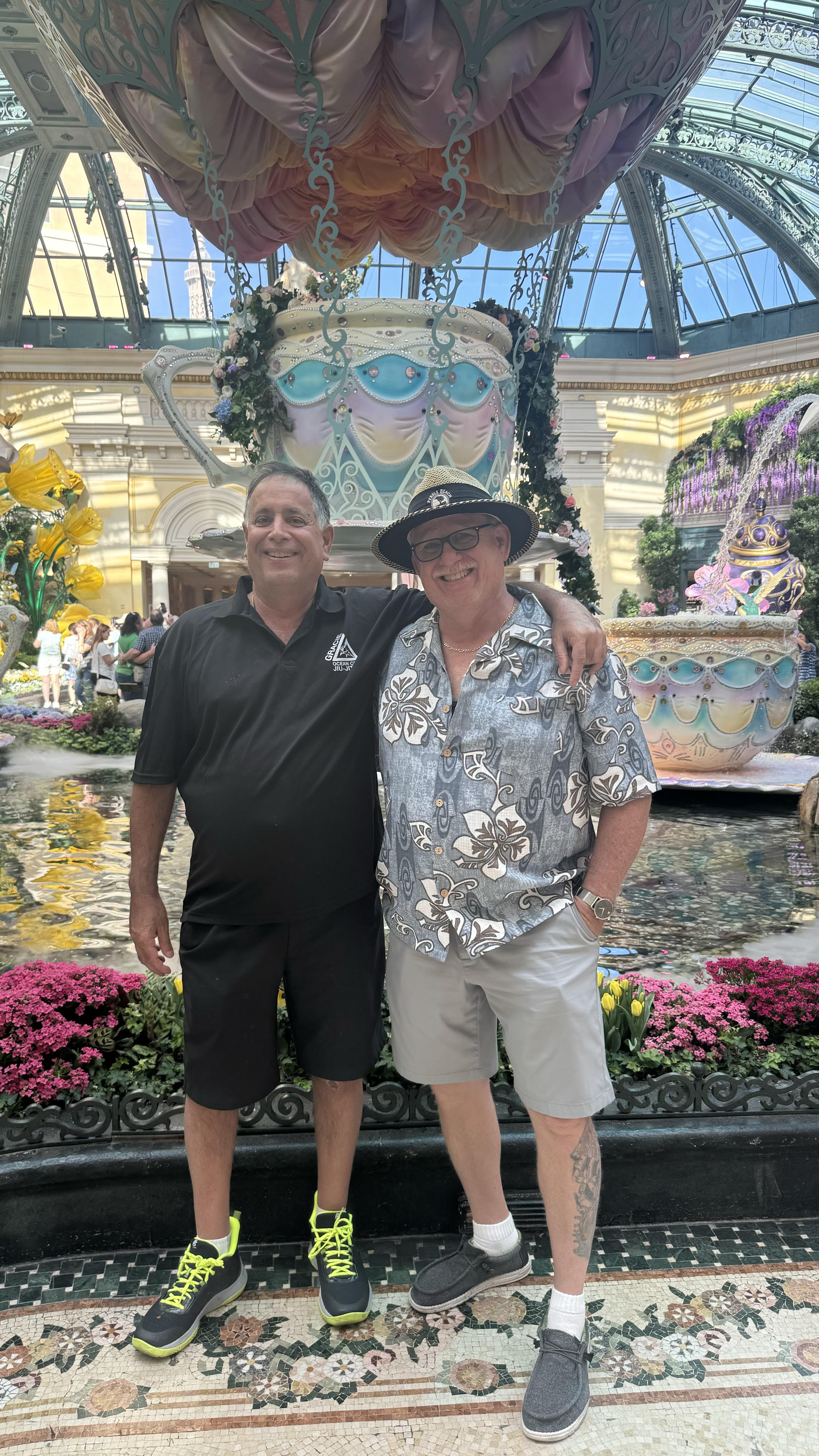 Two men pose for a picture next to a pond in a garden area in Las Vegas during daytime.