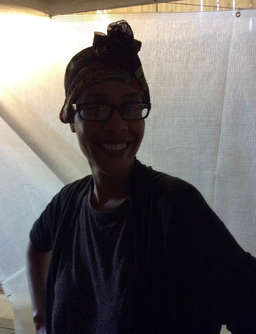 A person smiles while standing in a room with soft light in the background.