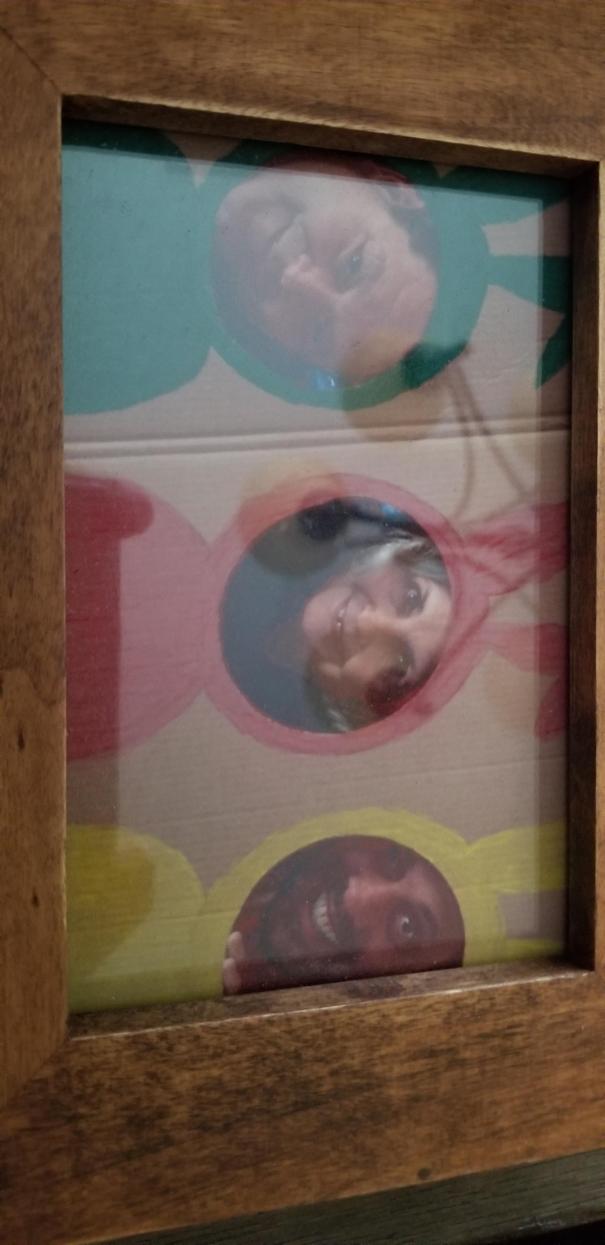 Children enjoy playing a game by looking through colorful openings in a board at a fair.