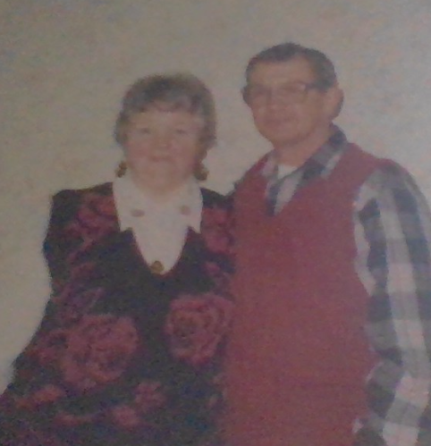 Older couple stands together indoors smiling and enjoying time spent during a casual gathering.