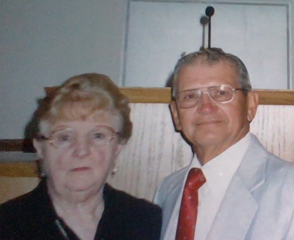 Couple poses for a picture at a community gathering wearing formal clothes with a backdrop.