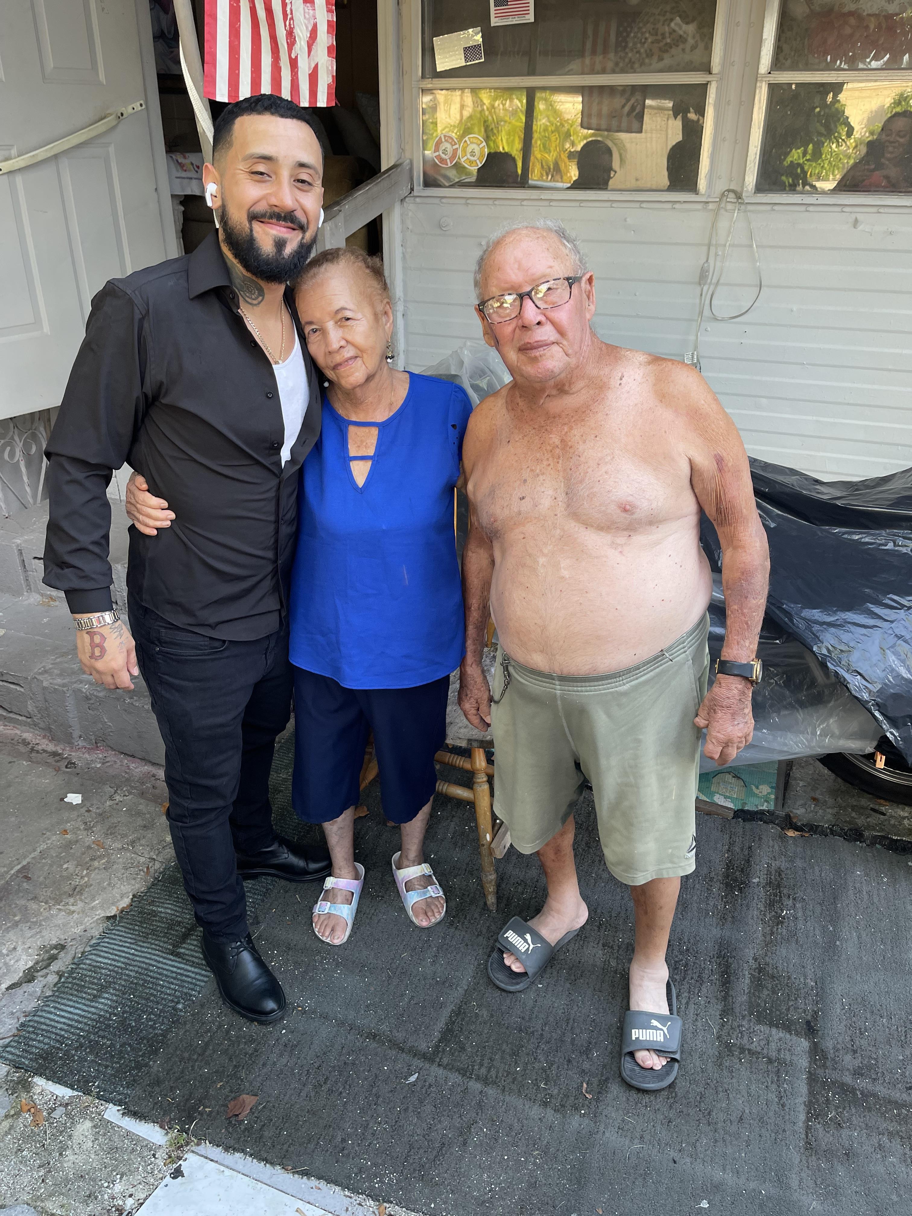 Three people stand close together in a neighborhood. They smile and look happy.