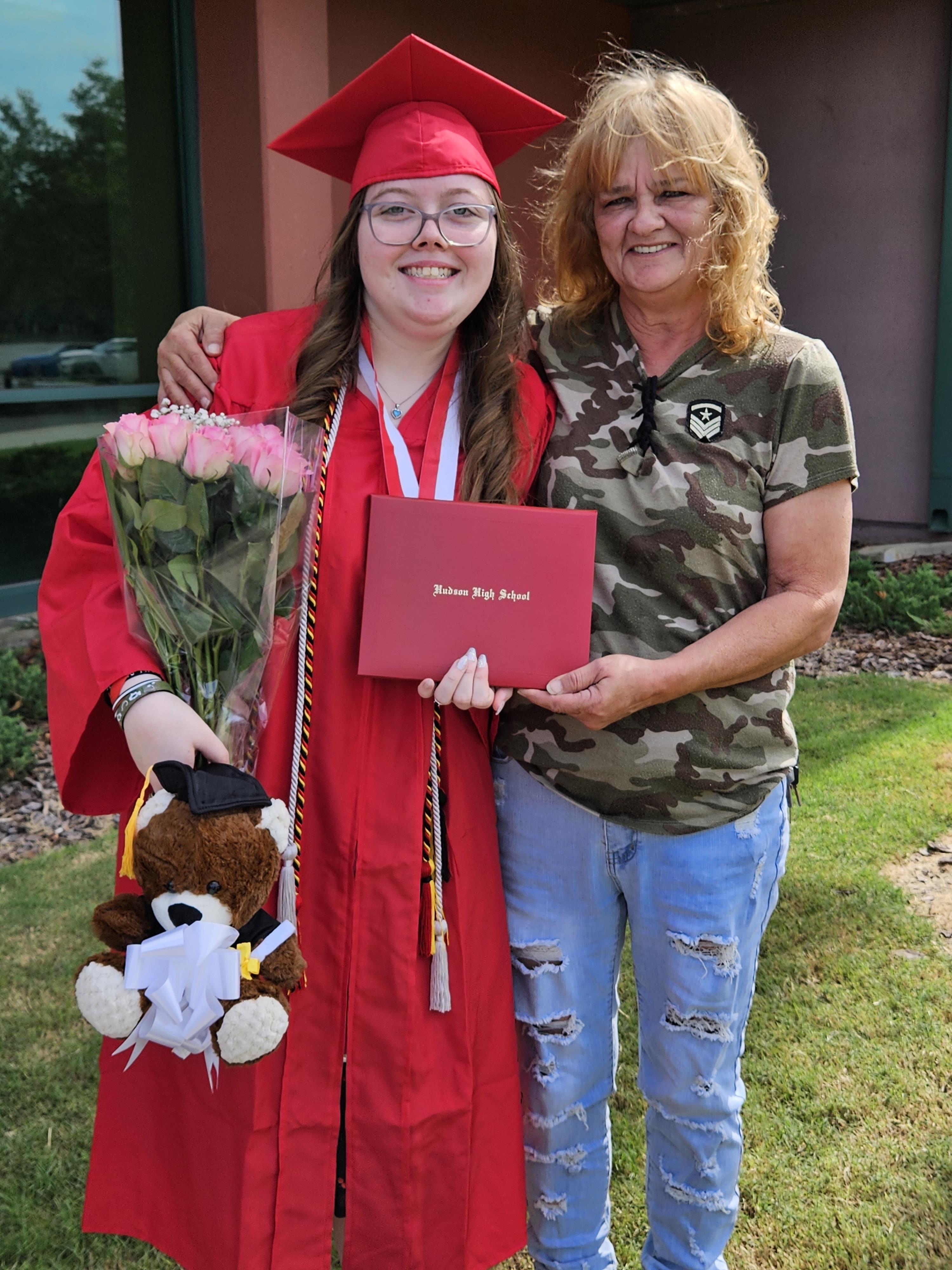 A woman in a cap and gown holding flowers and a teddy bear