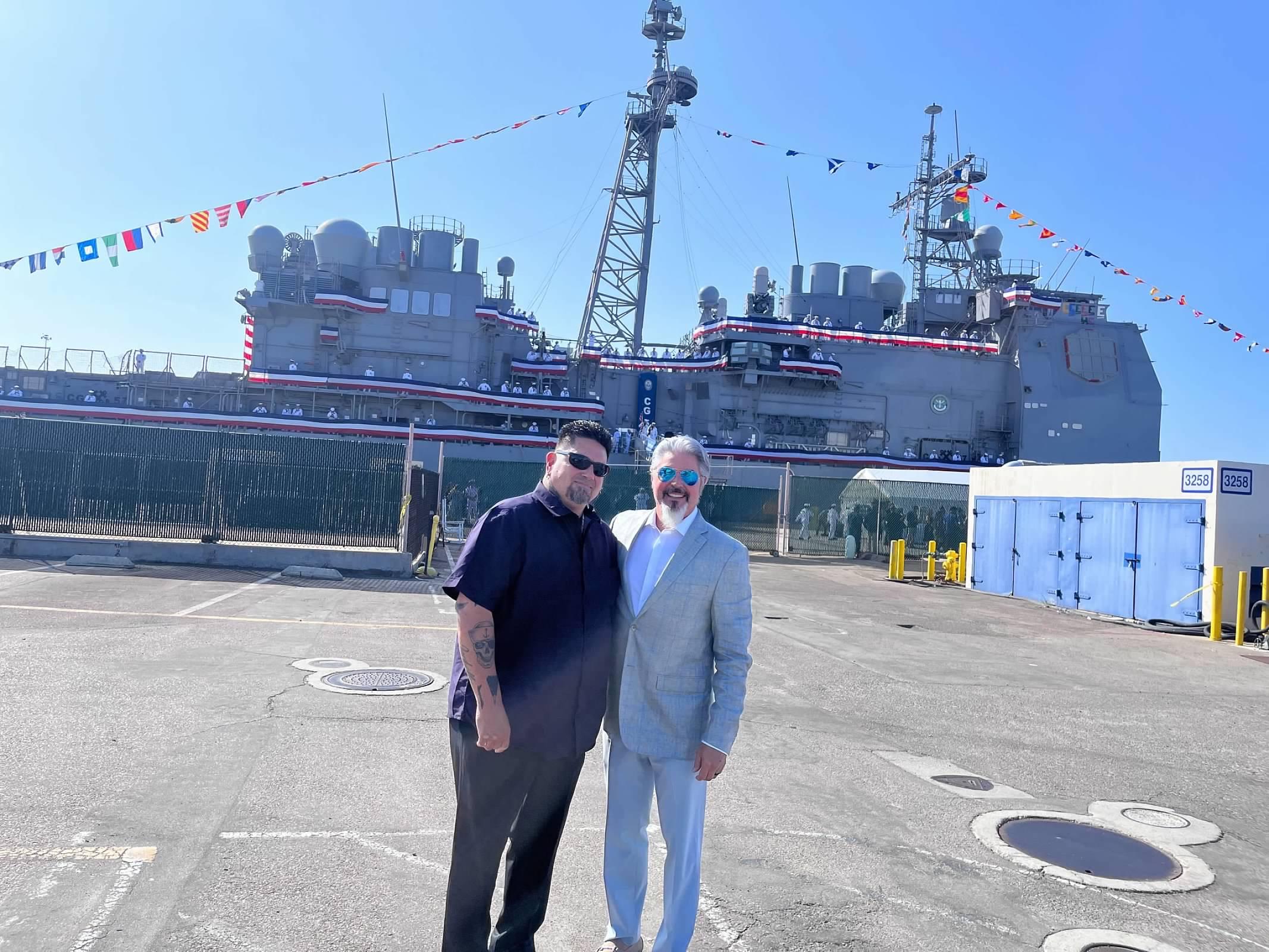 Two men standing in a parking lot with a large ship in the background