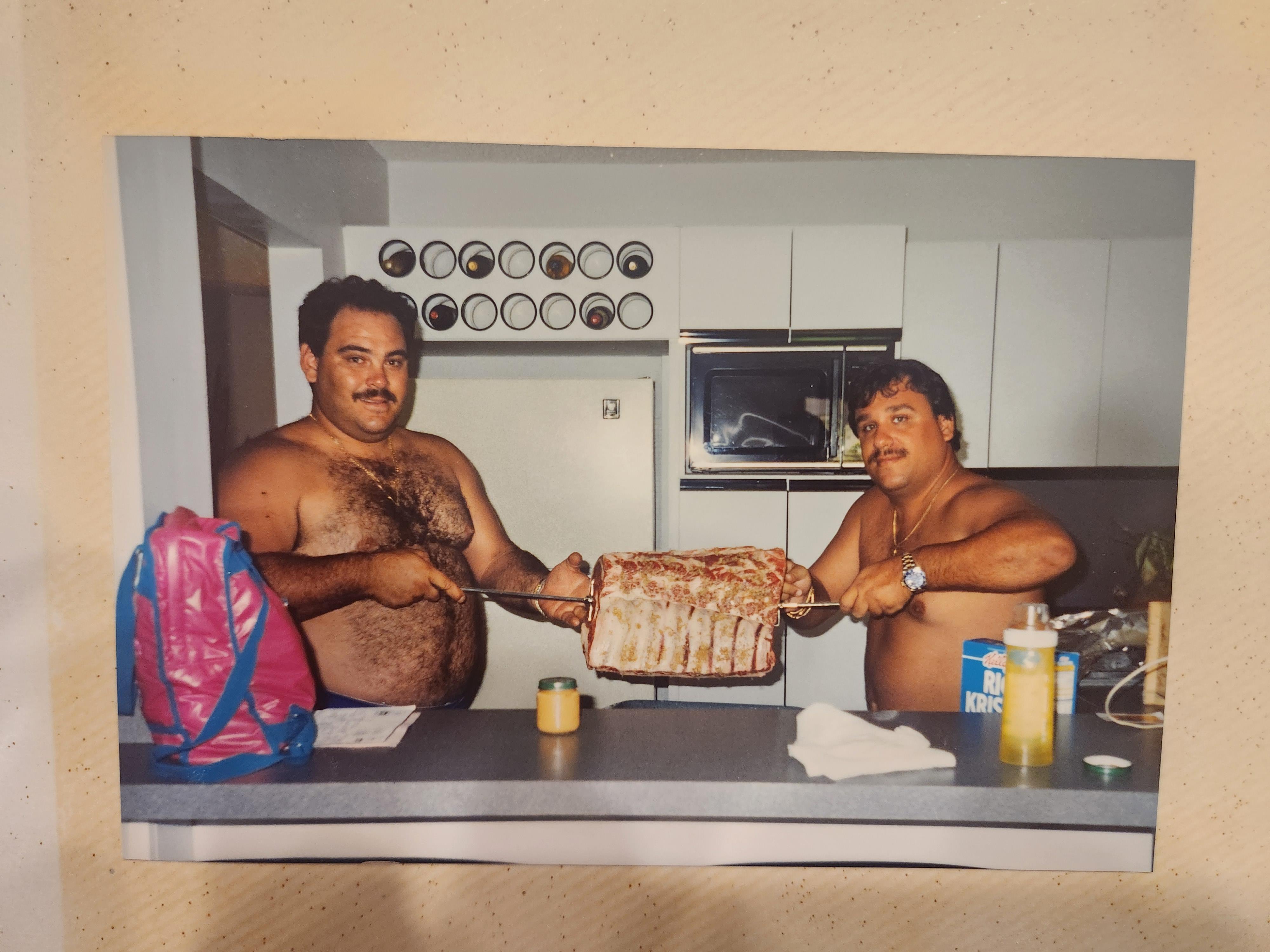 Two men holding meat on a barbeque