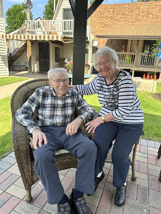 An old man and woman sitting on a chair outside