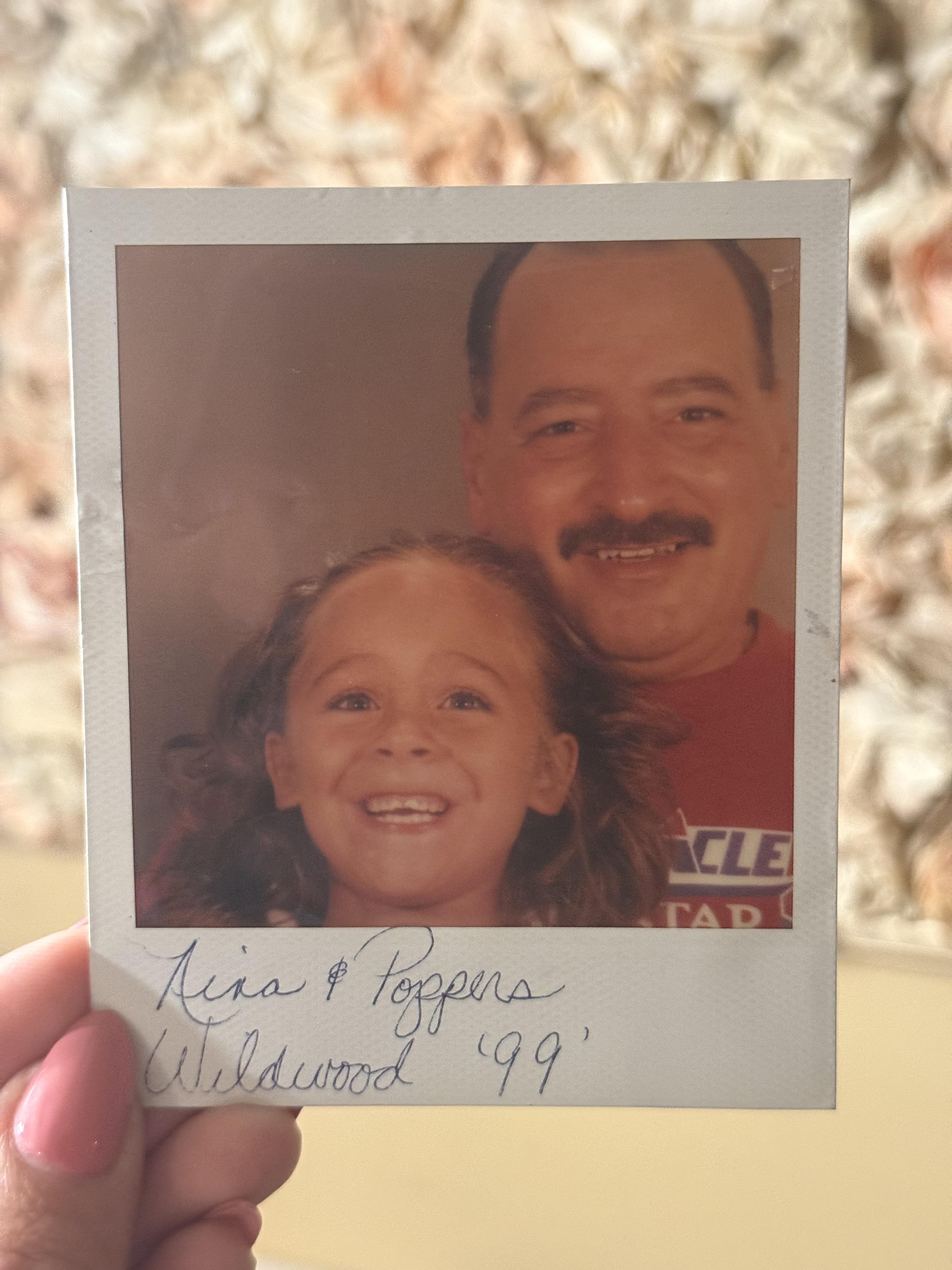A hand holding a polaroid of a man and a girl