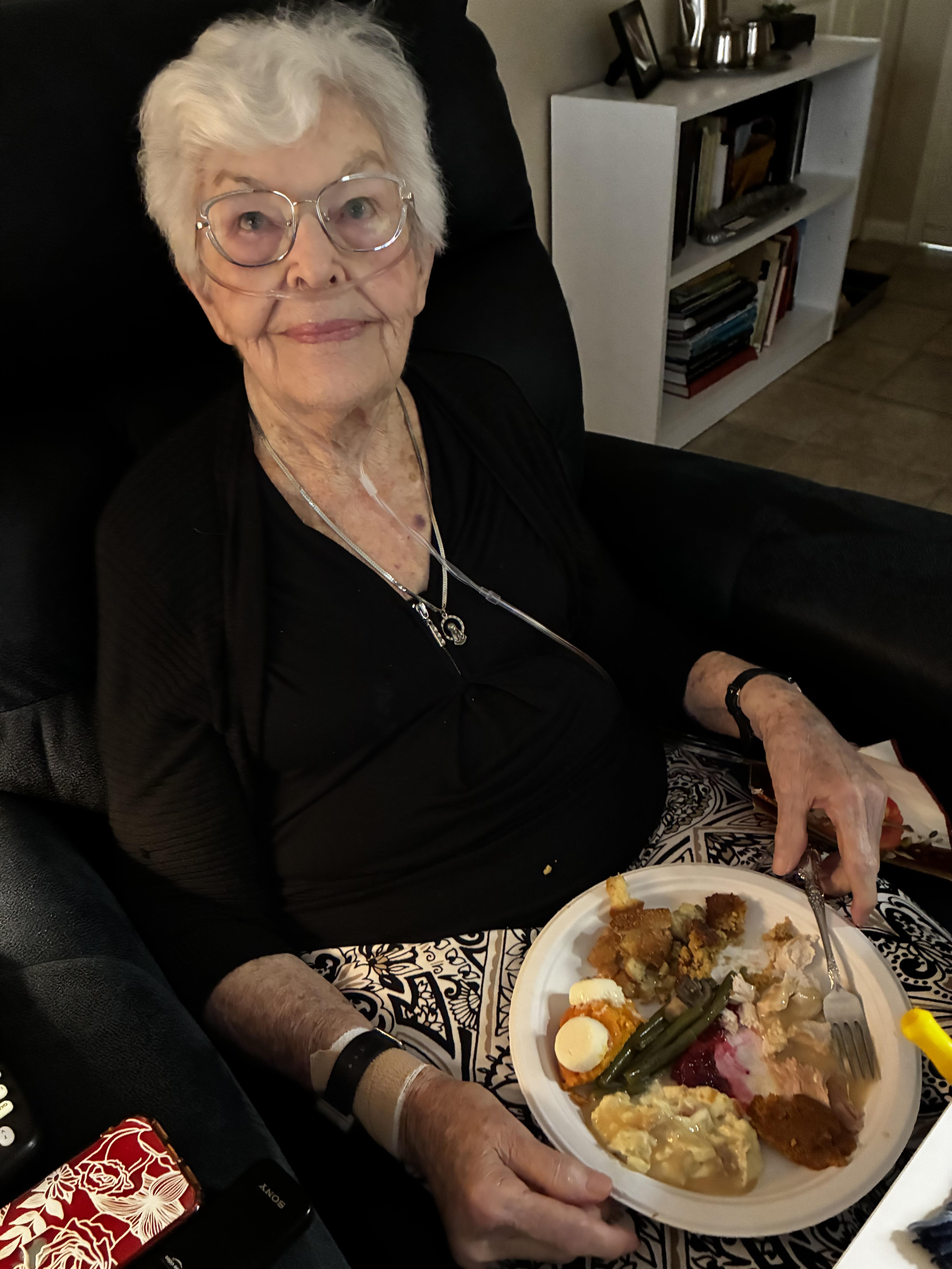 An old woman sitting in a chair with a plate of food