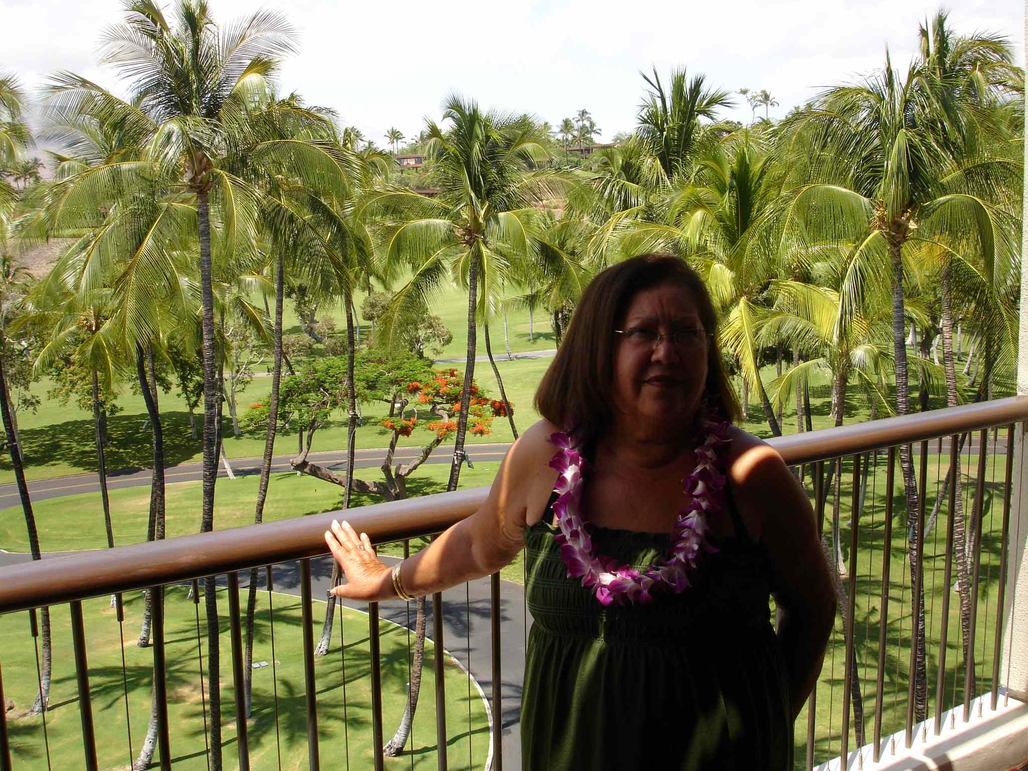 A woman standing on a balcony with palm trees in the background