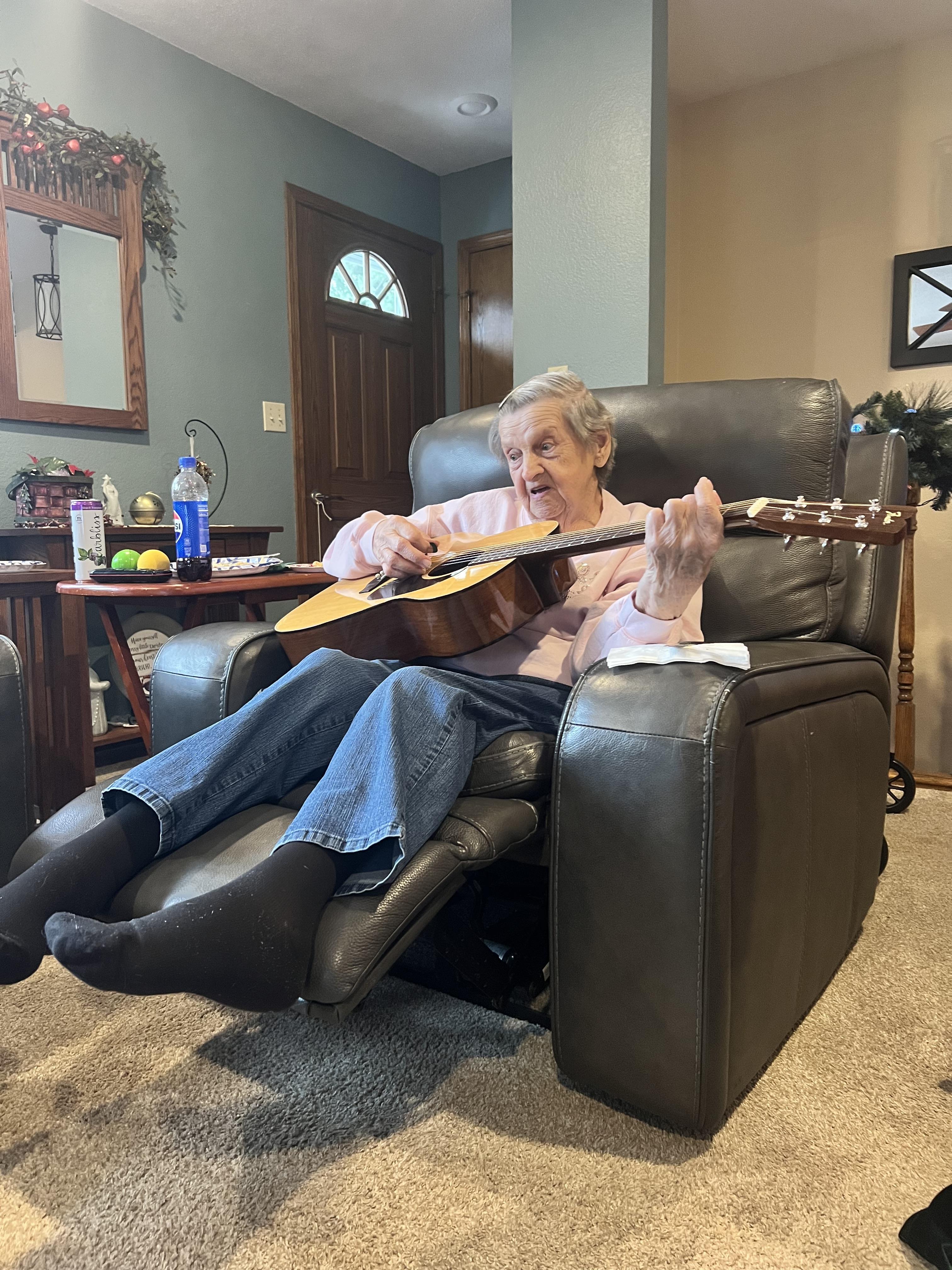 An old woman sitting in a chair playing a guitar