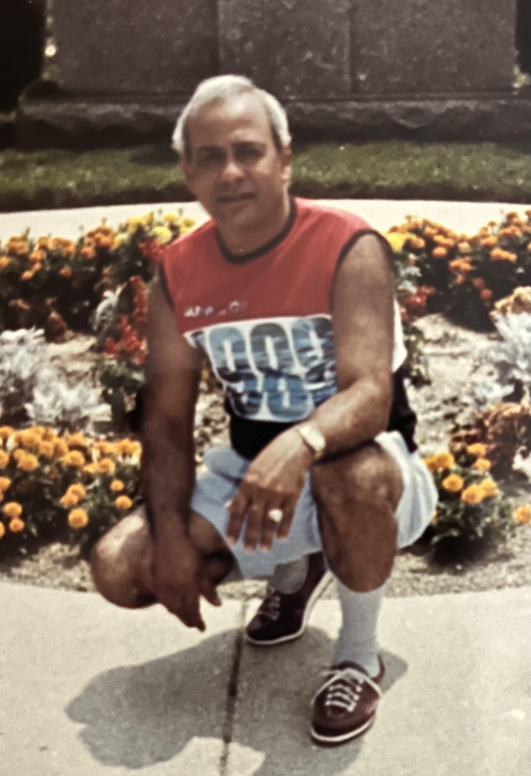 A man squatting in front of flowers