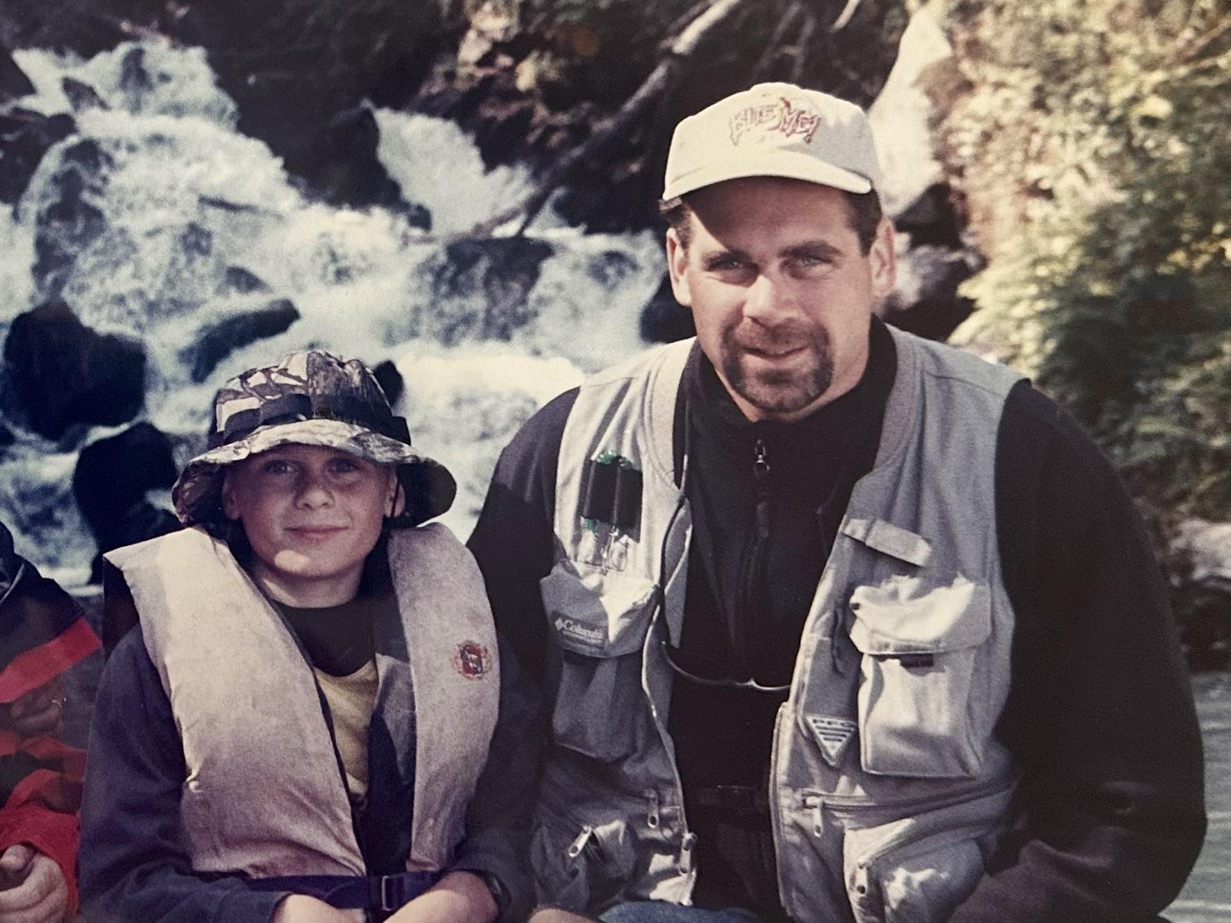 A man and boy sitting in front of a river