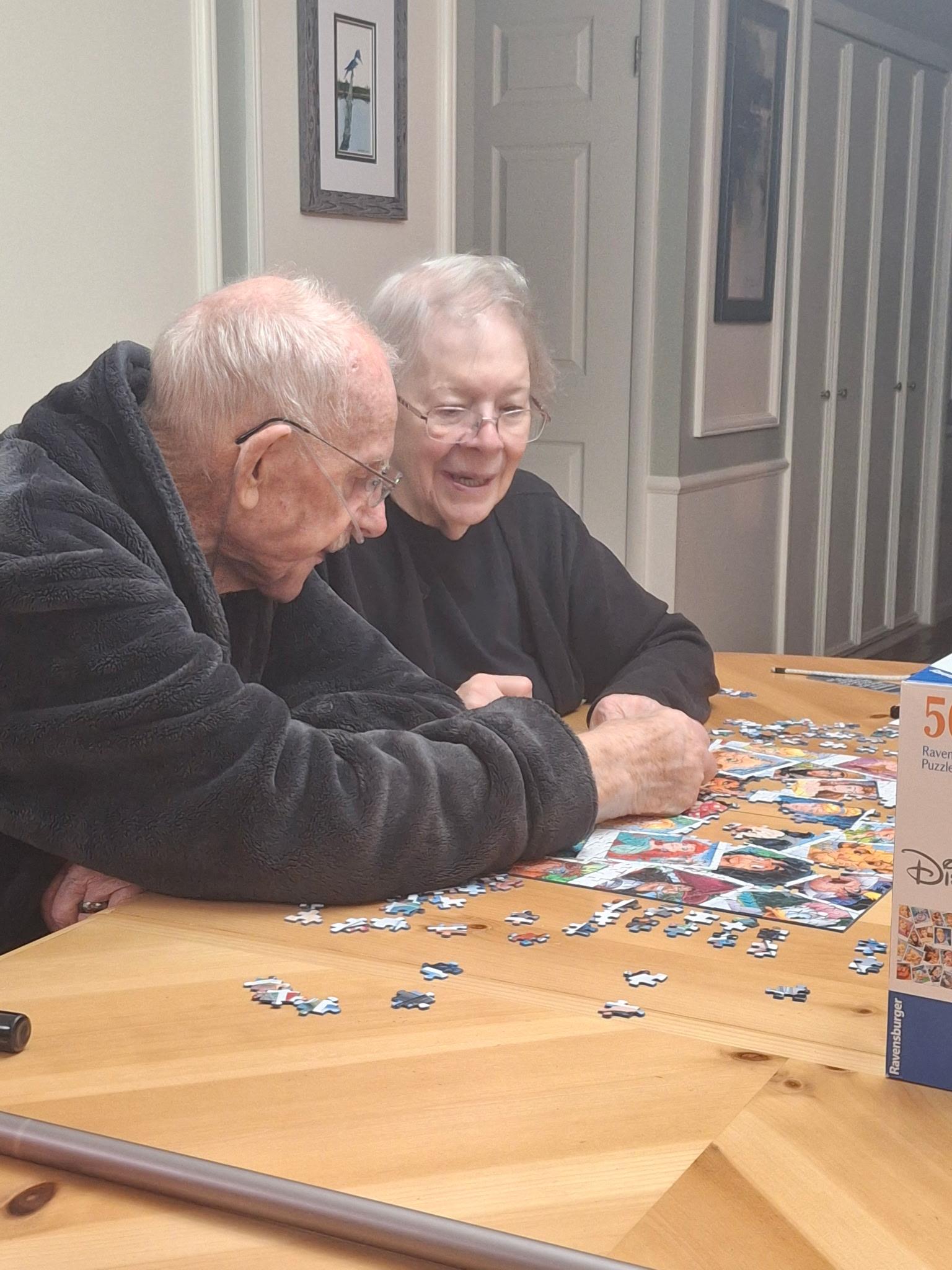 An old couple sitting at a table playing with puzzles