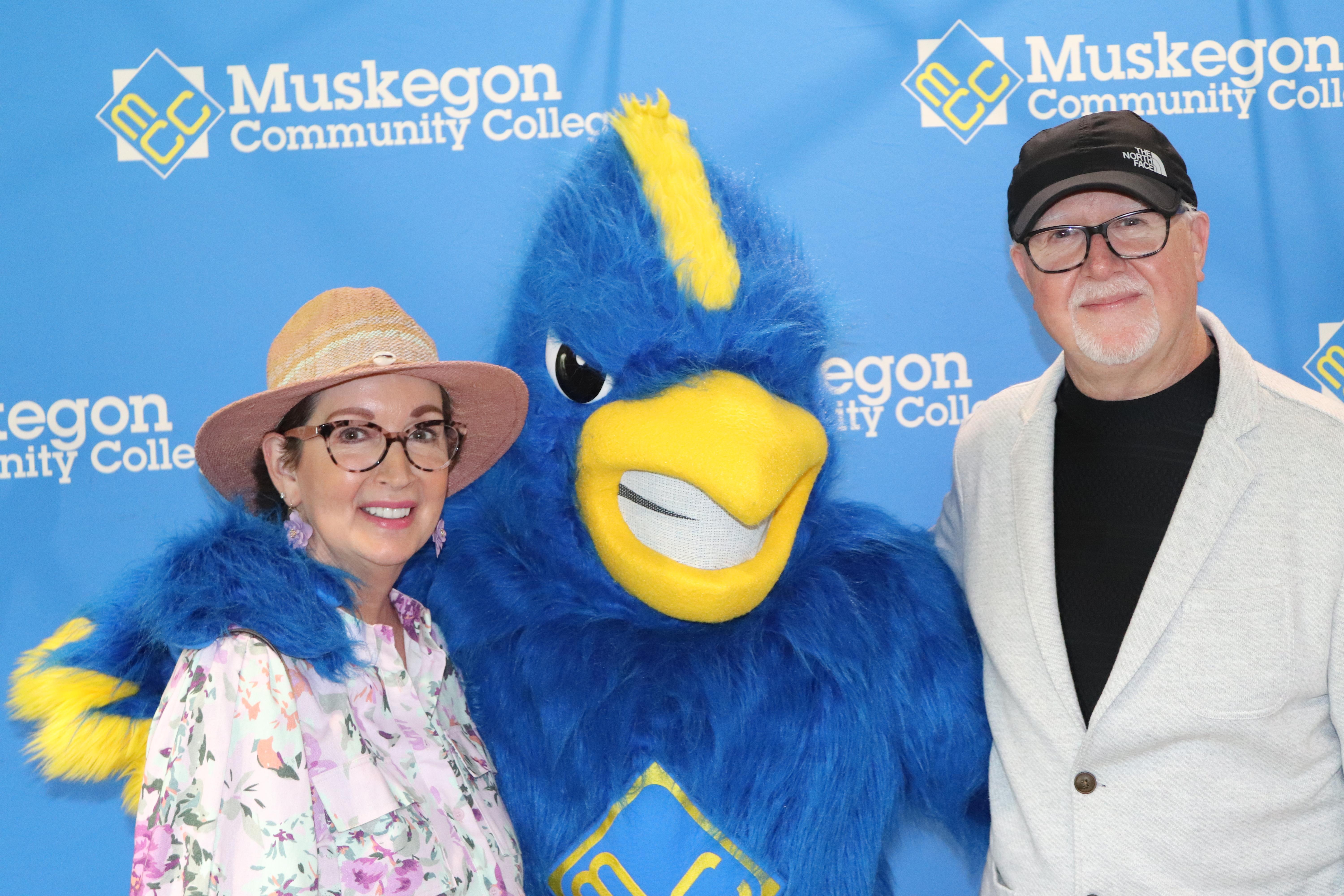 A man and woman standing next to a blue mascot