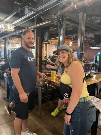 A man and woman standing in a room with tables and drinks