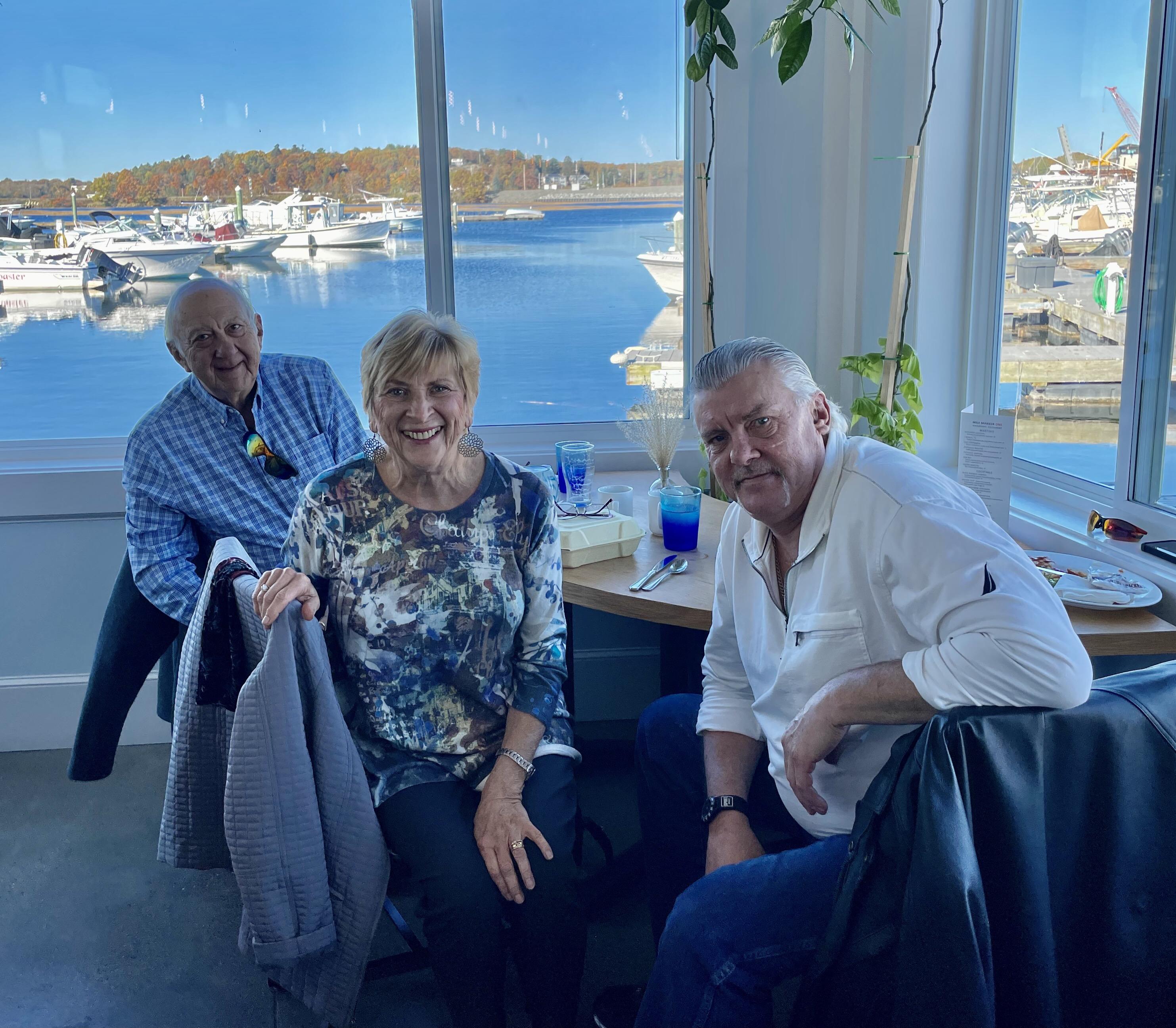 A group of people sitting in a room with a window and water in the background