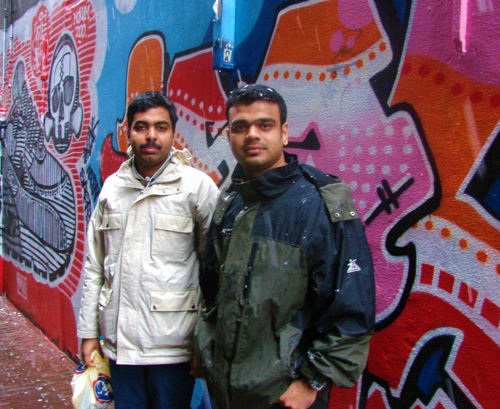 A couple of men standing in front of a wall with graffiti