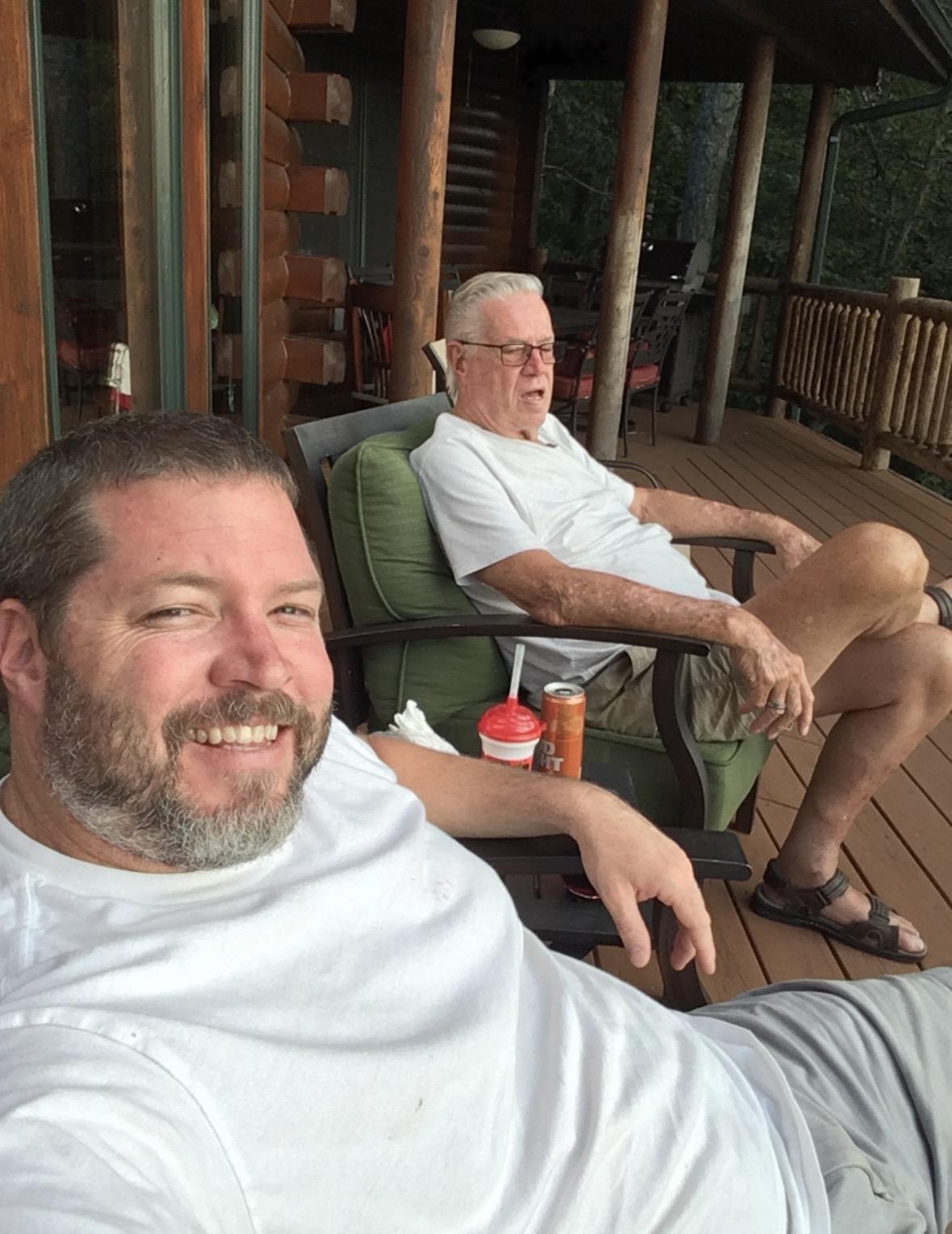 A man taking a selfie with another man sitting on chairs