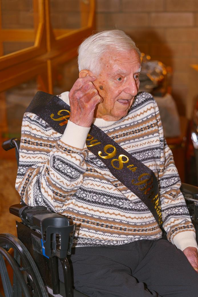 An old man in a wheelchair with a sash