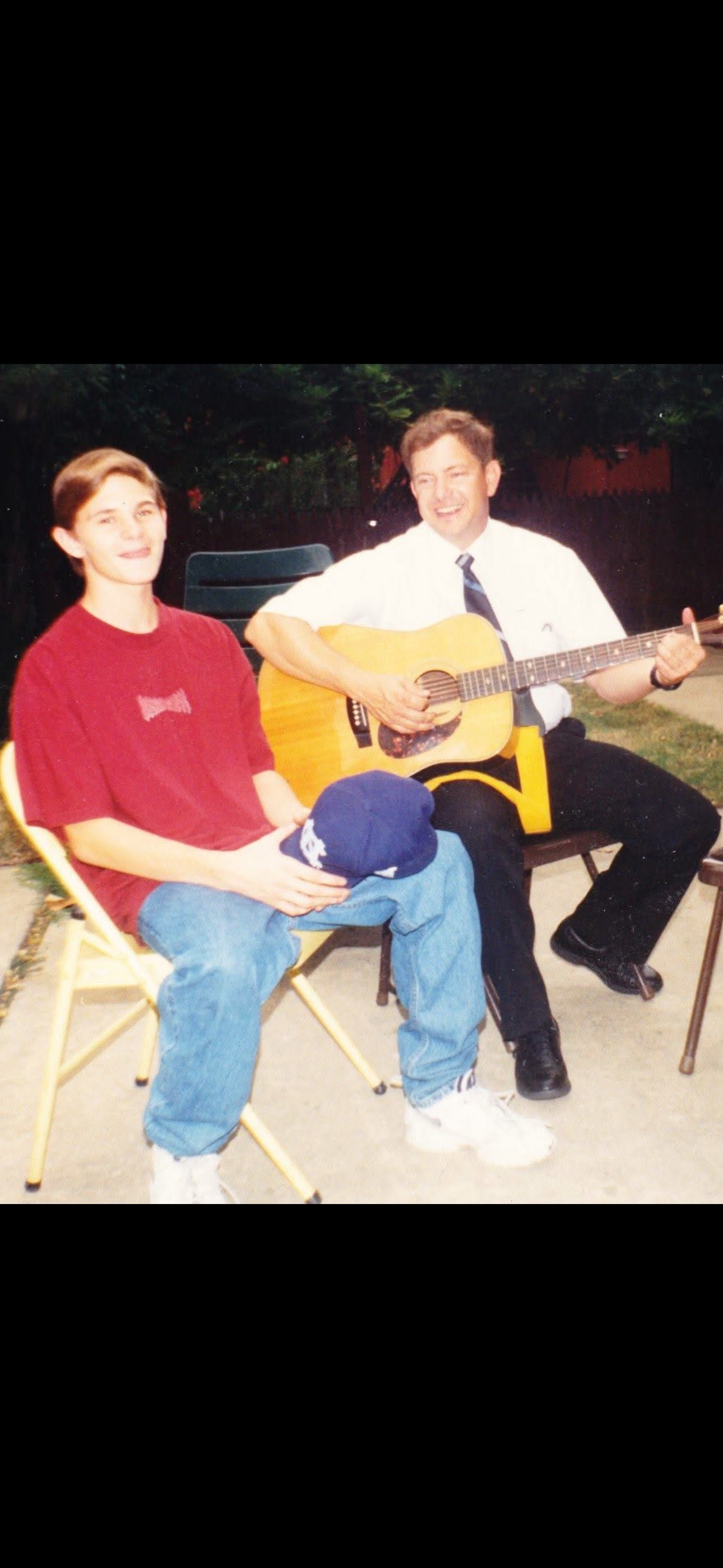 A man playing a guitar with a boy sitting in a chair