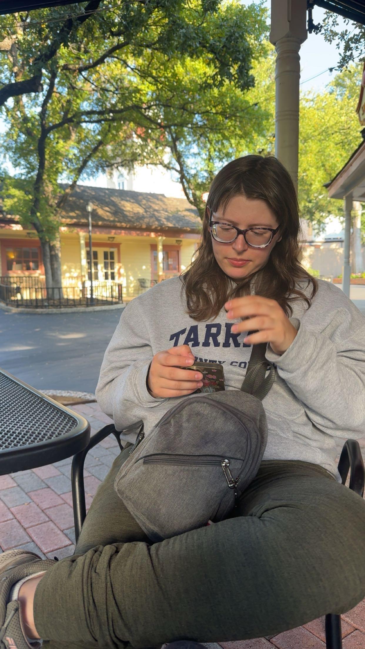 A woman sitting outside with a backpack and a phone