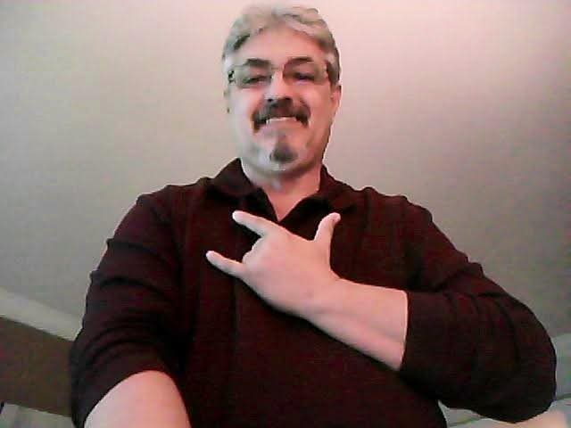 A man with a mustache and beard holding his hand up