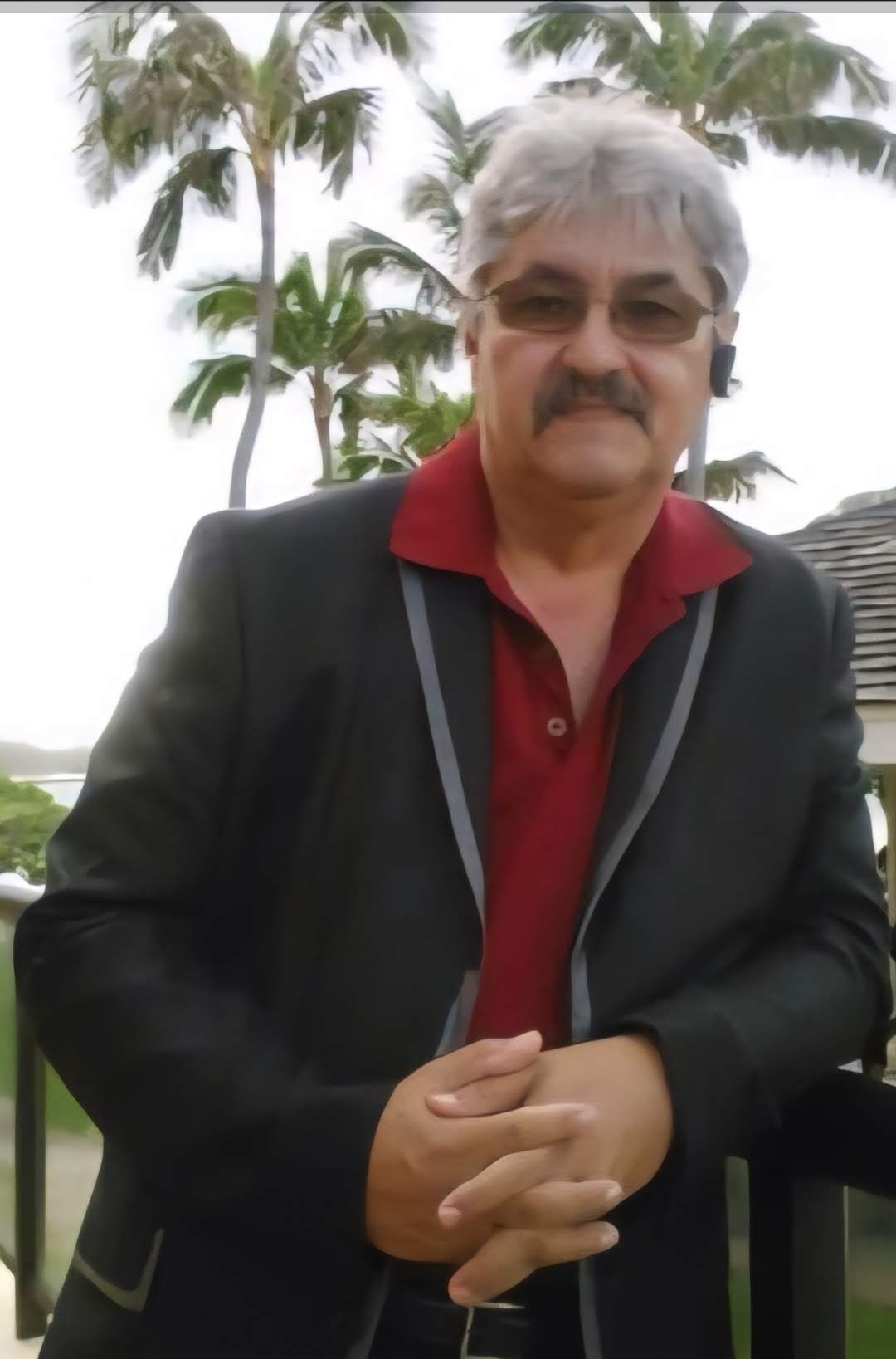 A man with a mustache wearing a black jacket and sunglasses