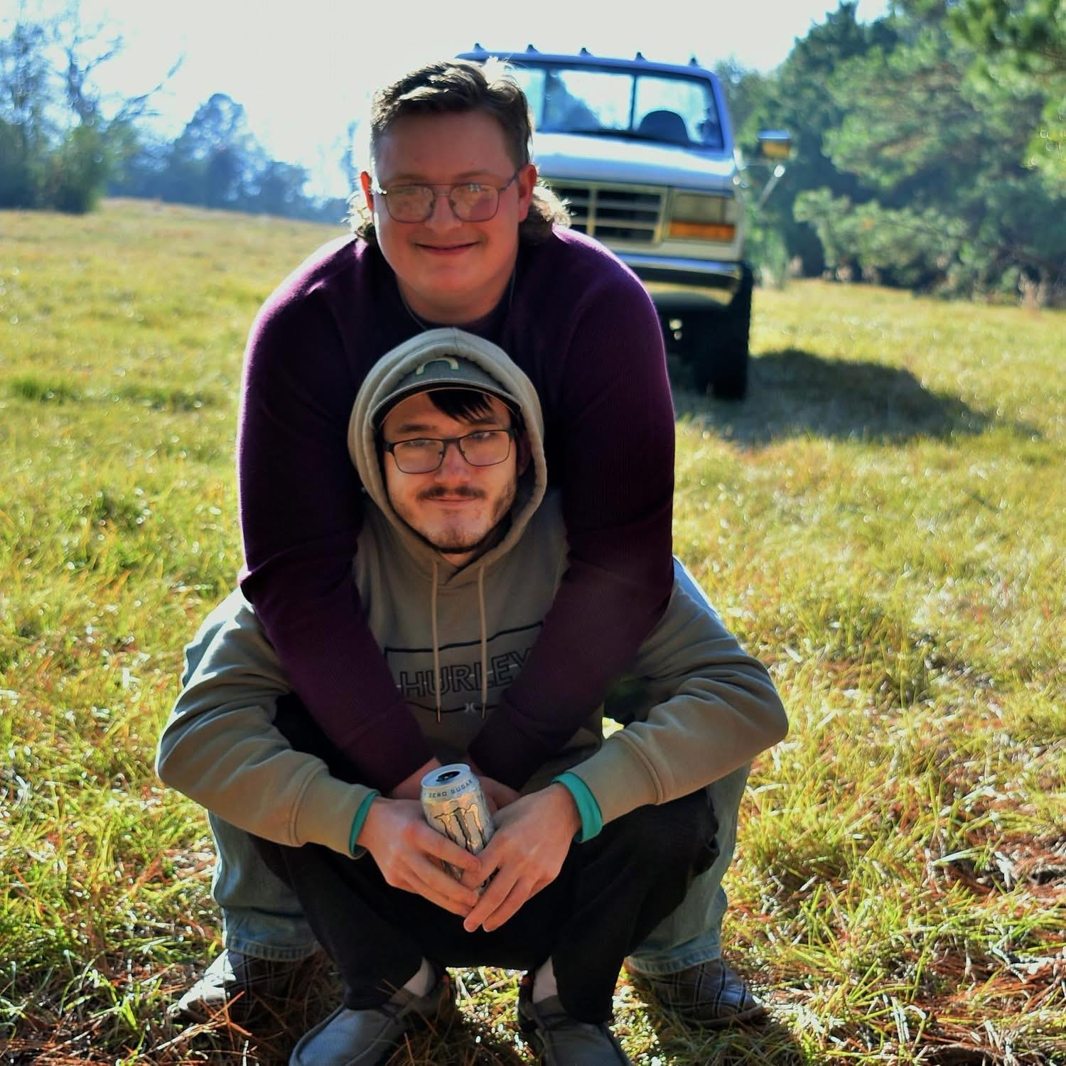 Two men kneeling on grass with a truck in the background