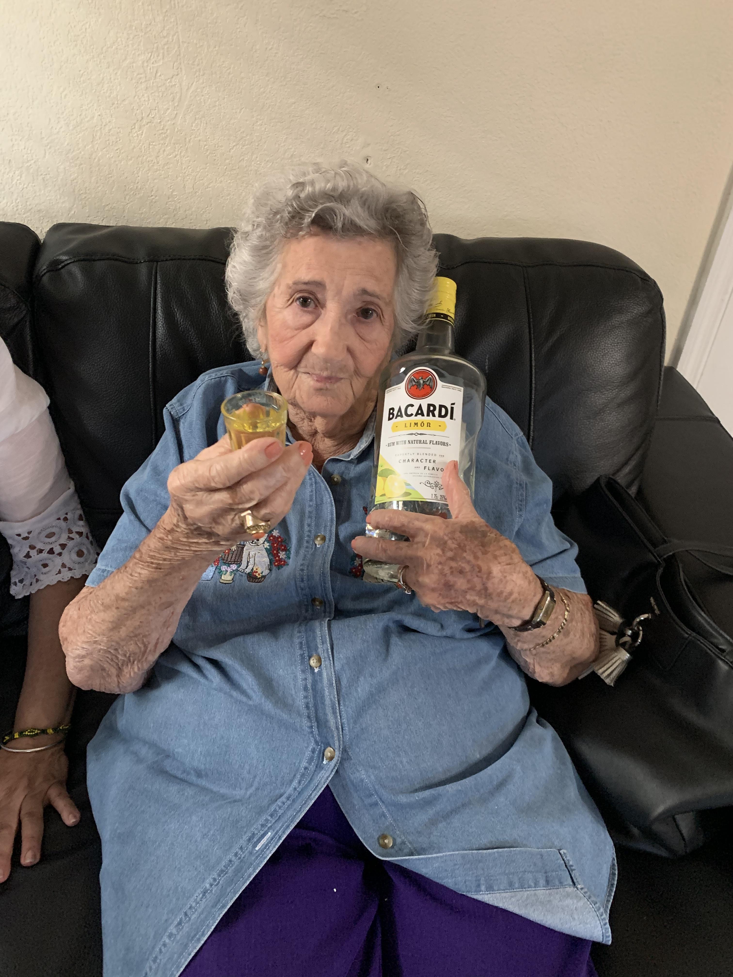 An old woman holding a glass and a bottle of alcohol