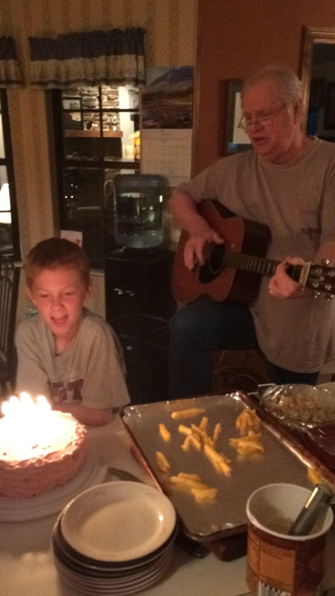 A man playing guitar and a boy sitting at a table with food and a cake