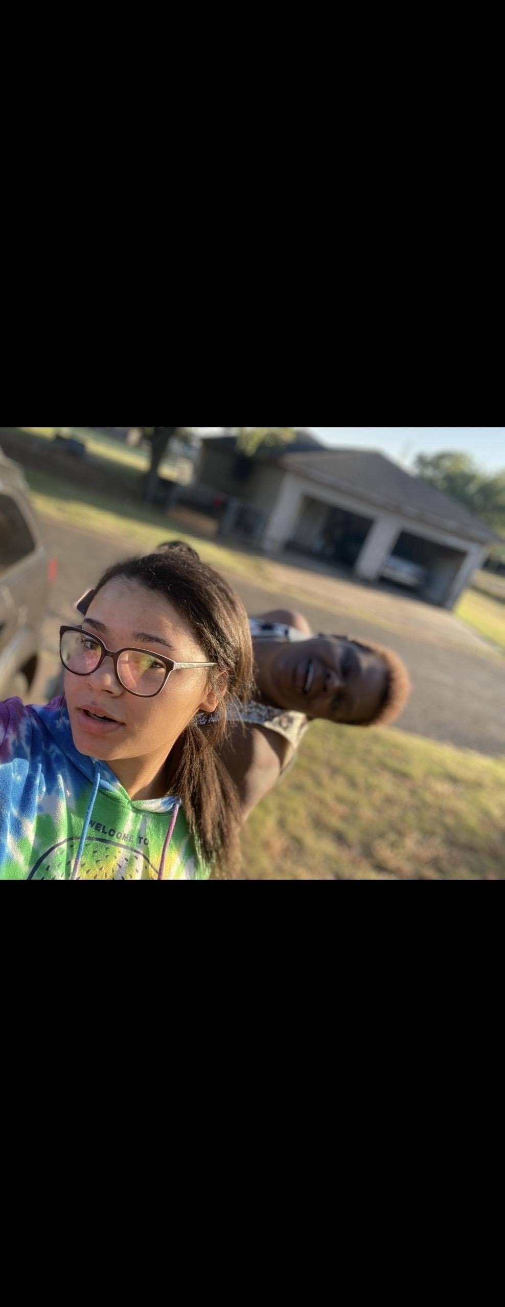 A woman taking a selfie with a man behind her