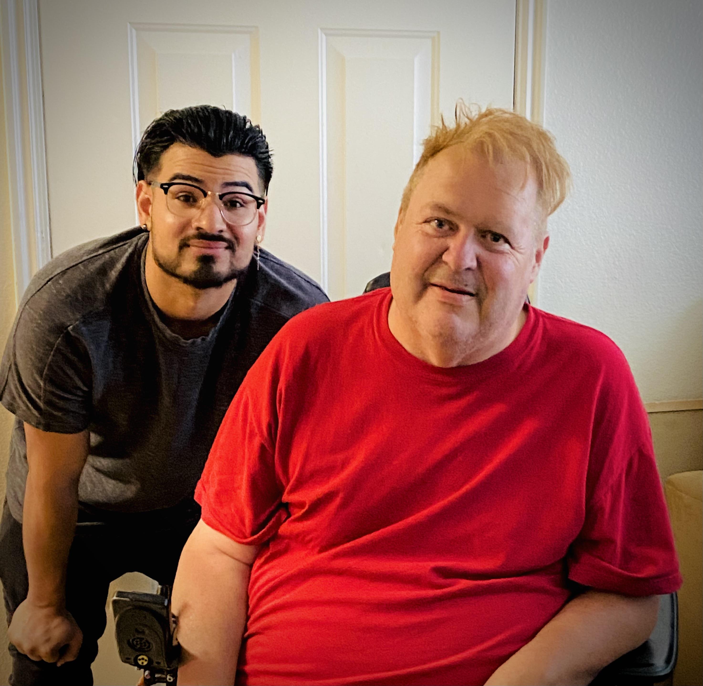 A man standing next to a man in a chair