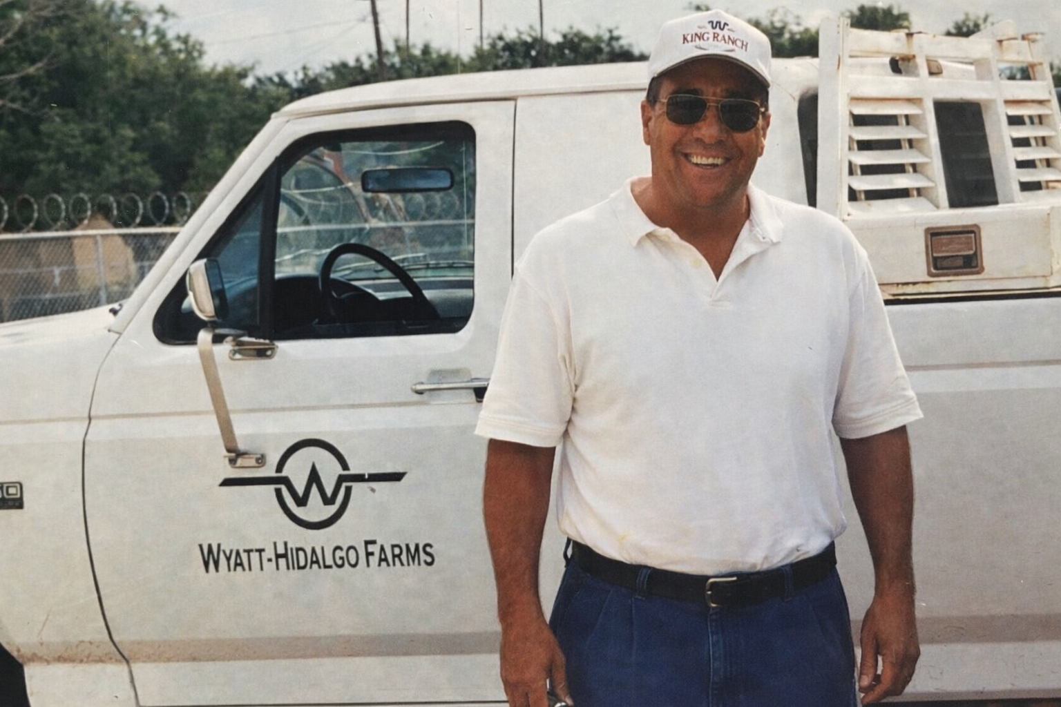 A man in a white shirt and cap standing in front of a white truck