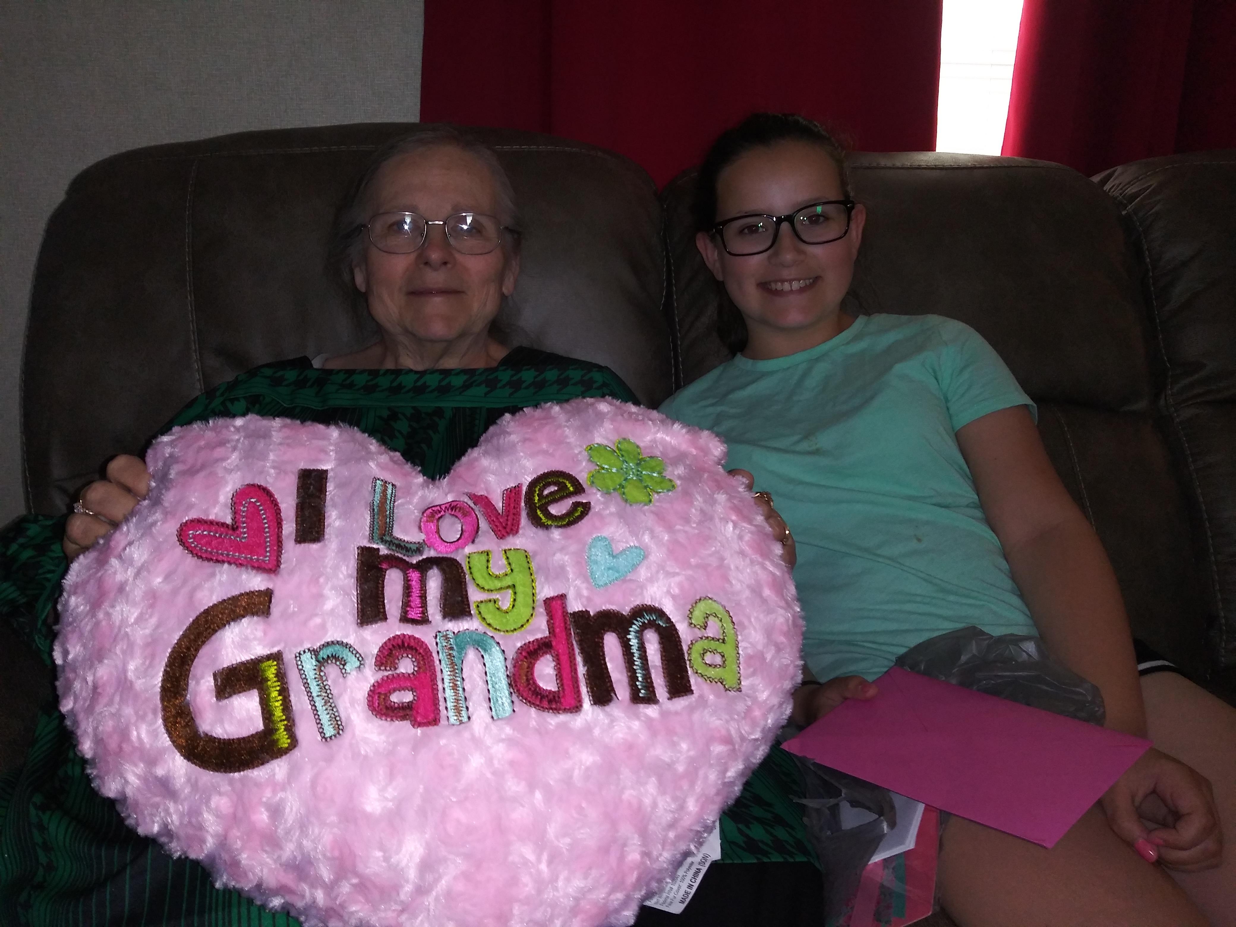 A woman and a young girl sitting on a couch with a heart shaped pillow