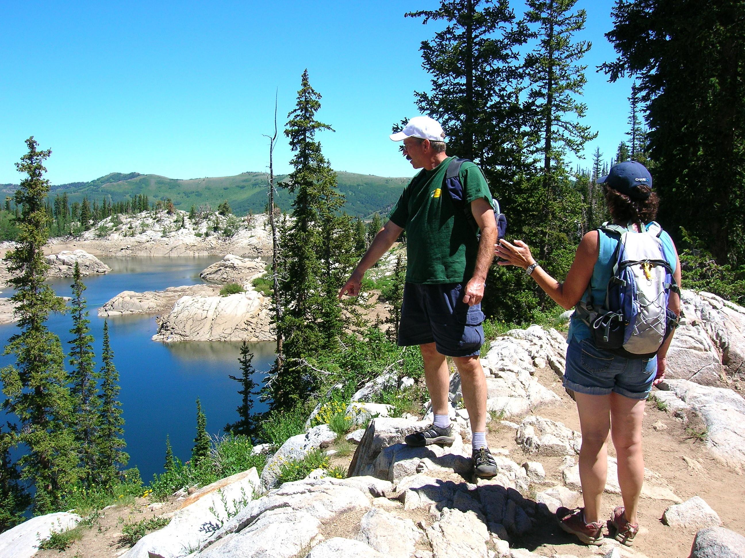 A man and woman standing on a rocky cliff overlooking a lake