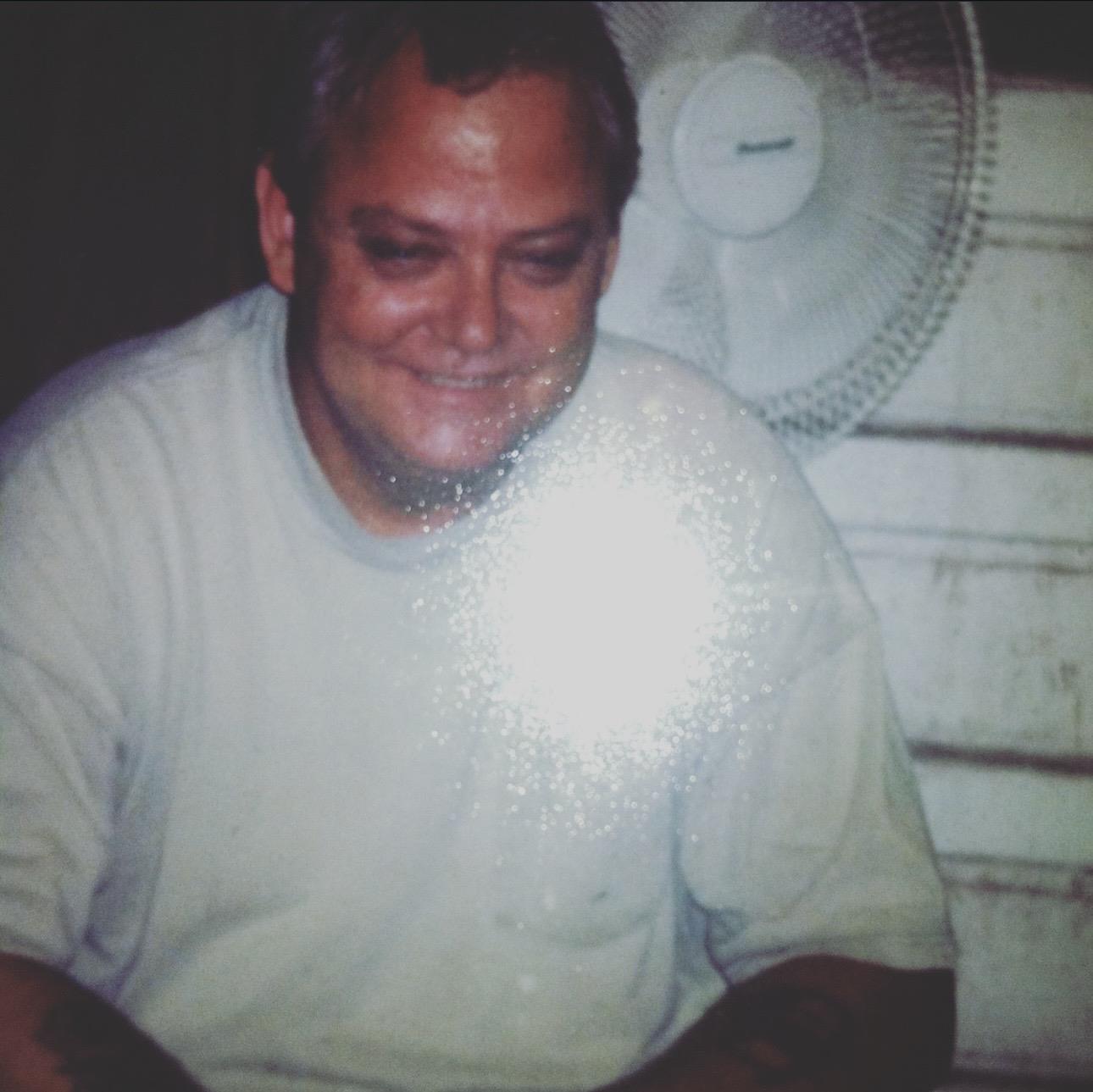 A man smiling with a bright light shining on his chest