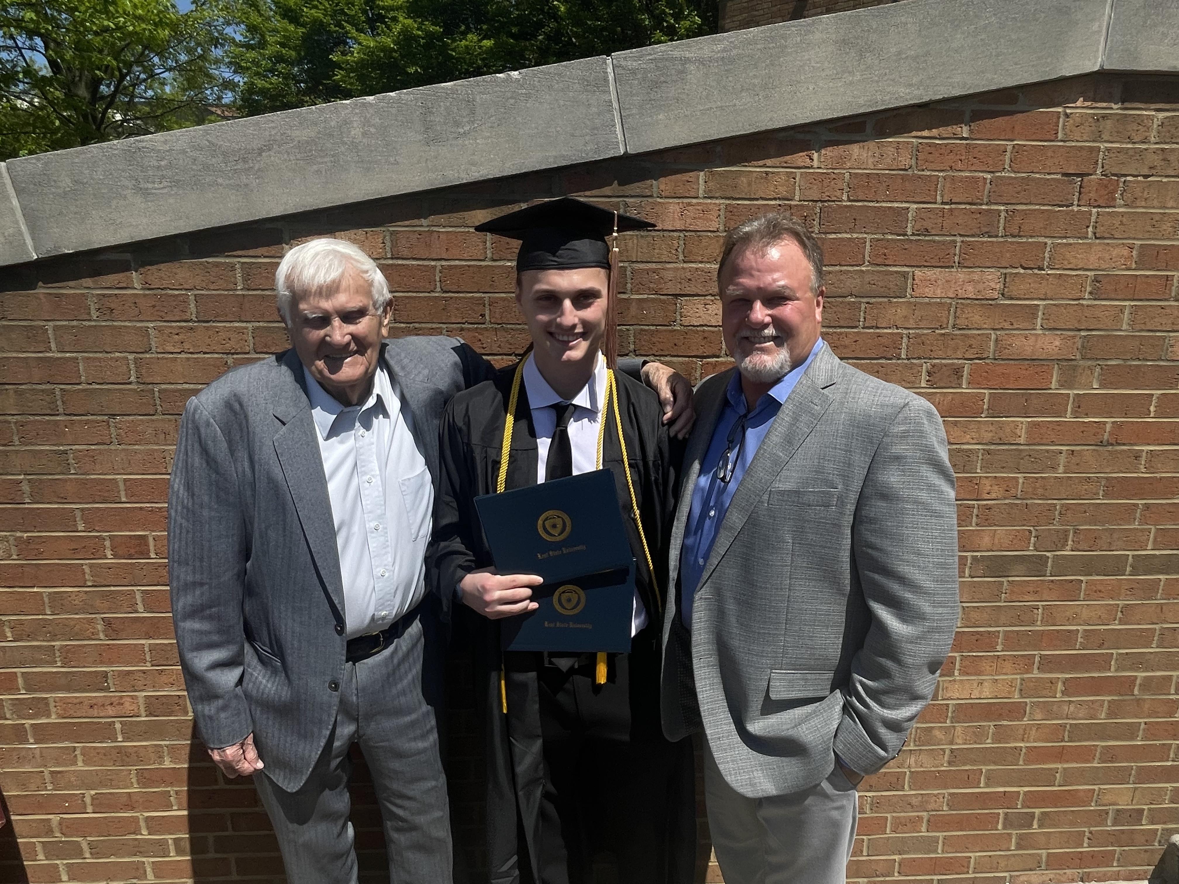 A man in a graduation cap and gown standing next to a man in a suit