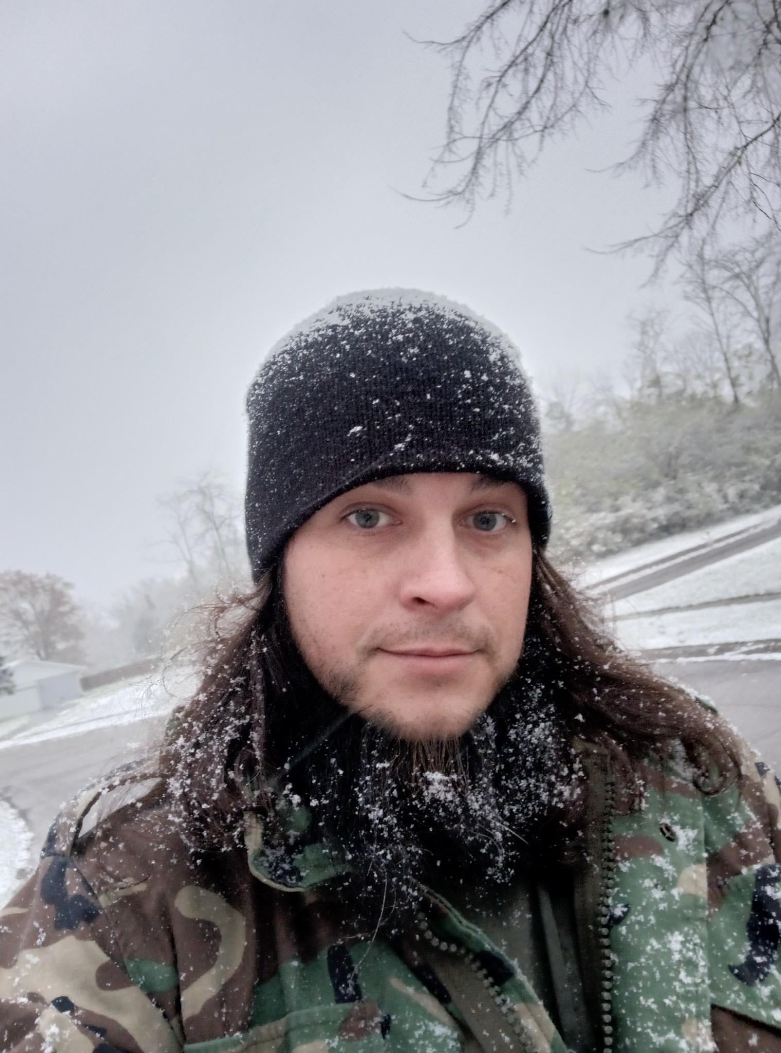 A man with long hair and a beard in a hat and snow