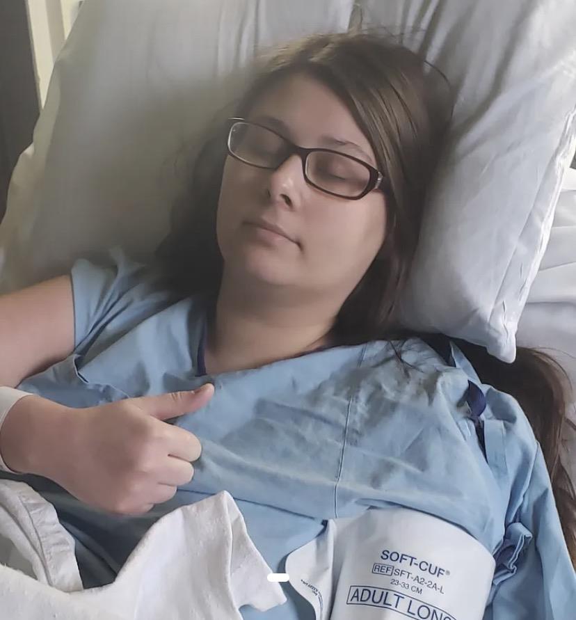 A woman lying in a hospital bed pointing at her