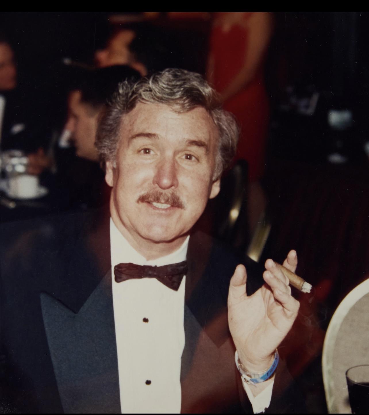 A man in a tuxedo holding a cigar