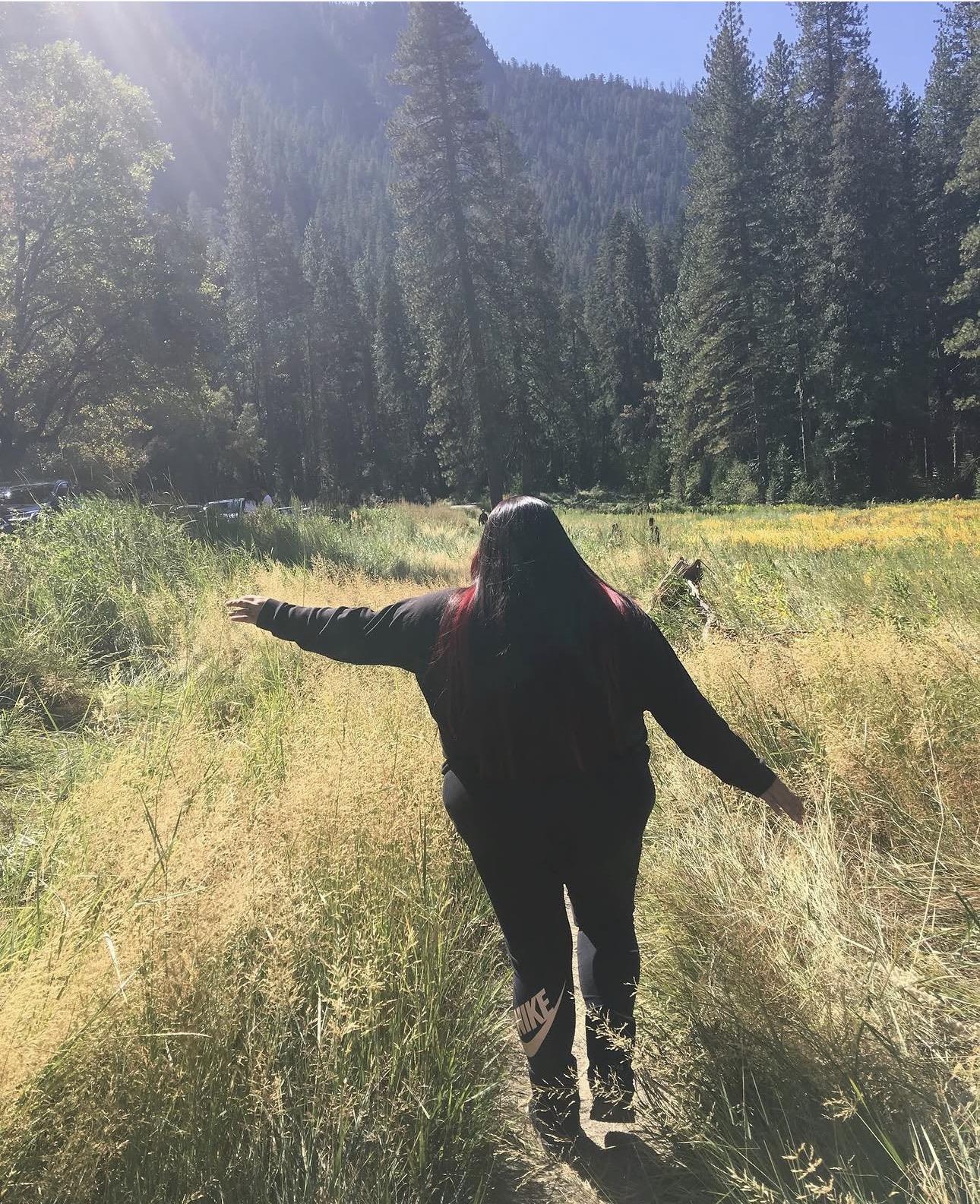 A woman walking in a field with tall grass and trees